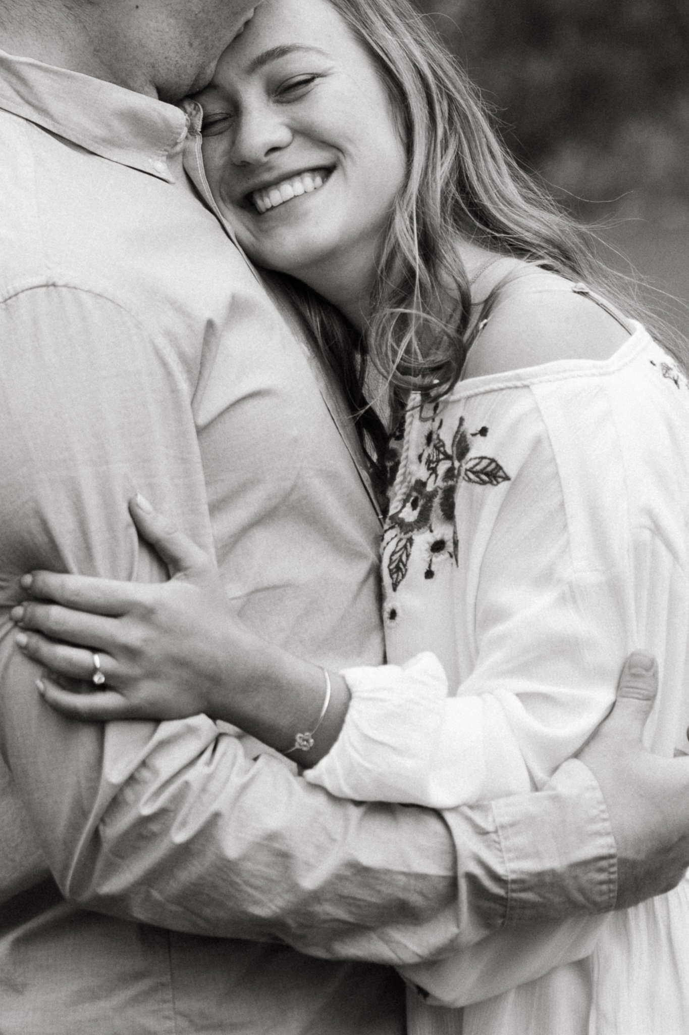 A woman embracing a man, smiling with her eyes closed and showing her wedding ring, in black and white.