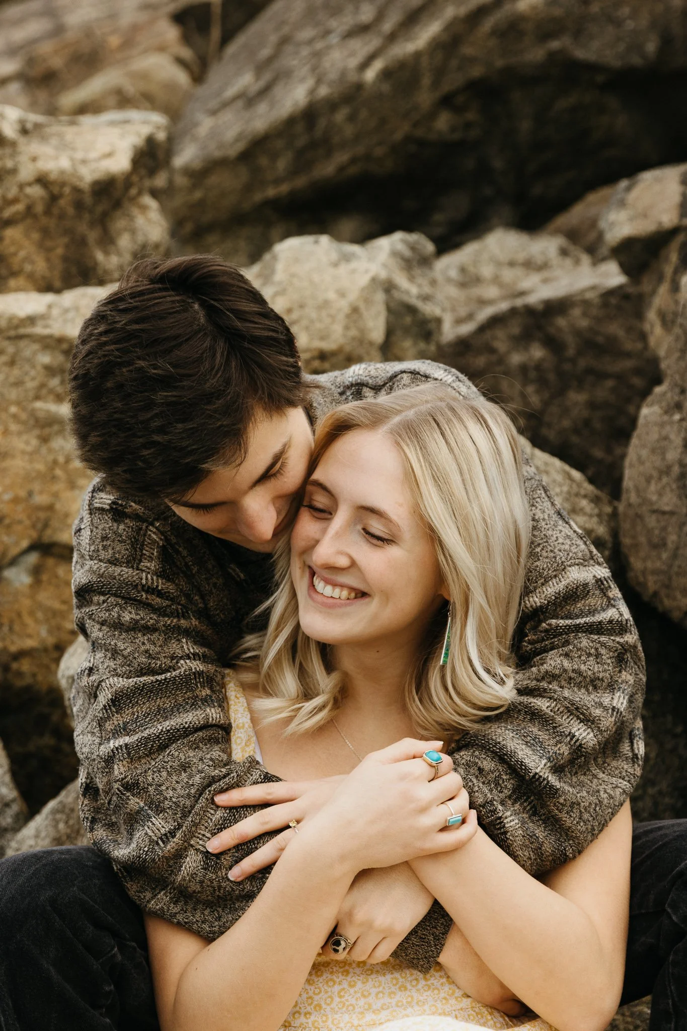 A man and a woman sharing a warm embrace outdoors among rocks, smiling and happy.