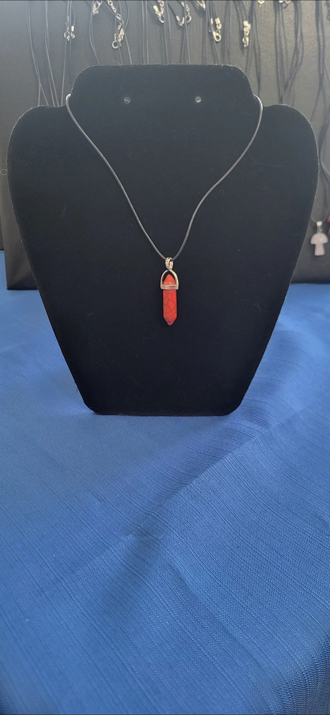 Red gemstone necklace with silver chain on a black display bust, with various jewelry in the background.