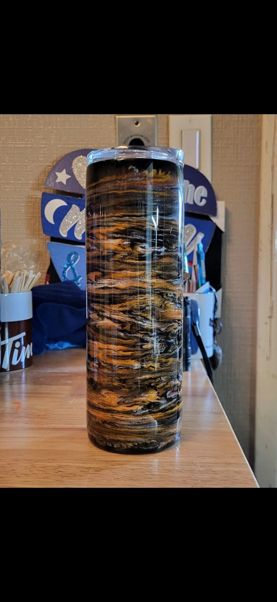 A cylindrical object with a marbled pattern of black, brown, yellow, and white colors, placed on a wooden surface in a cozy, decorated room.