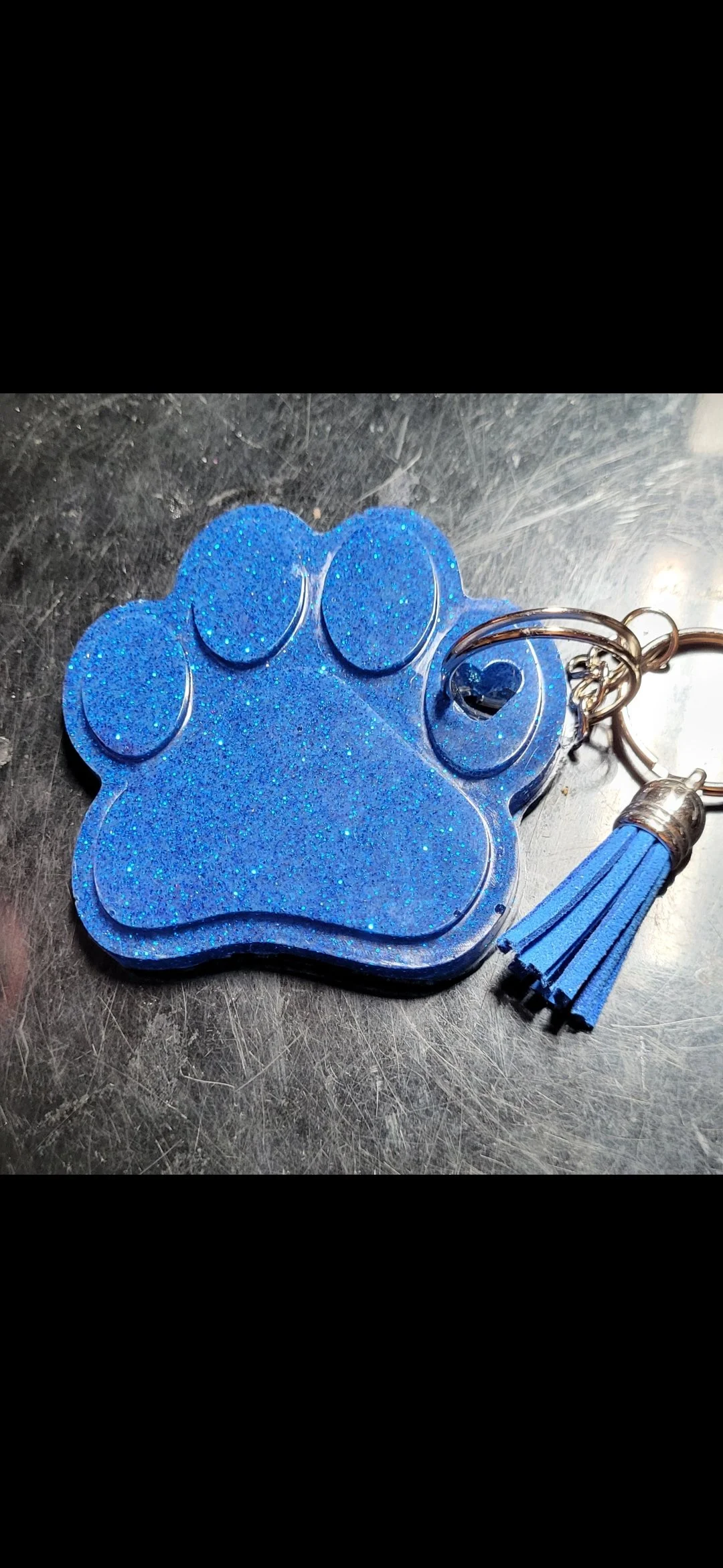 Blue glitter paw print keychain with a matching blue tassel on a metallic surface
