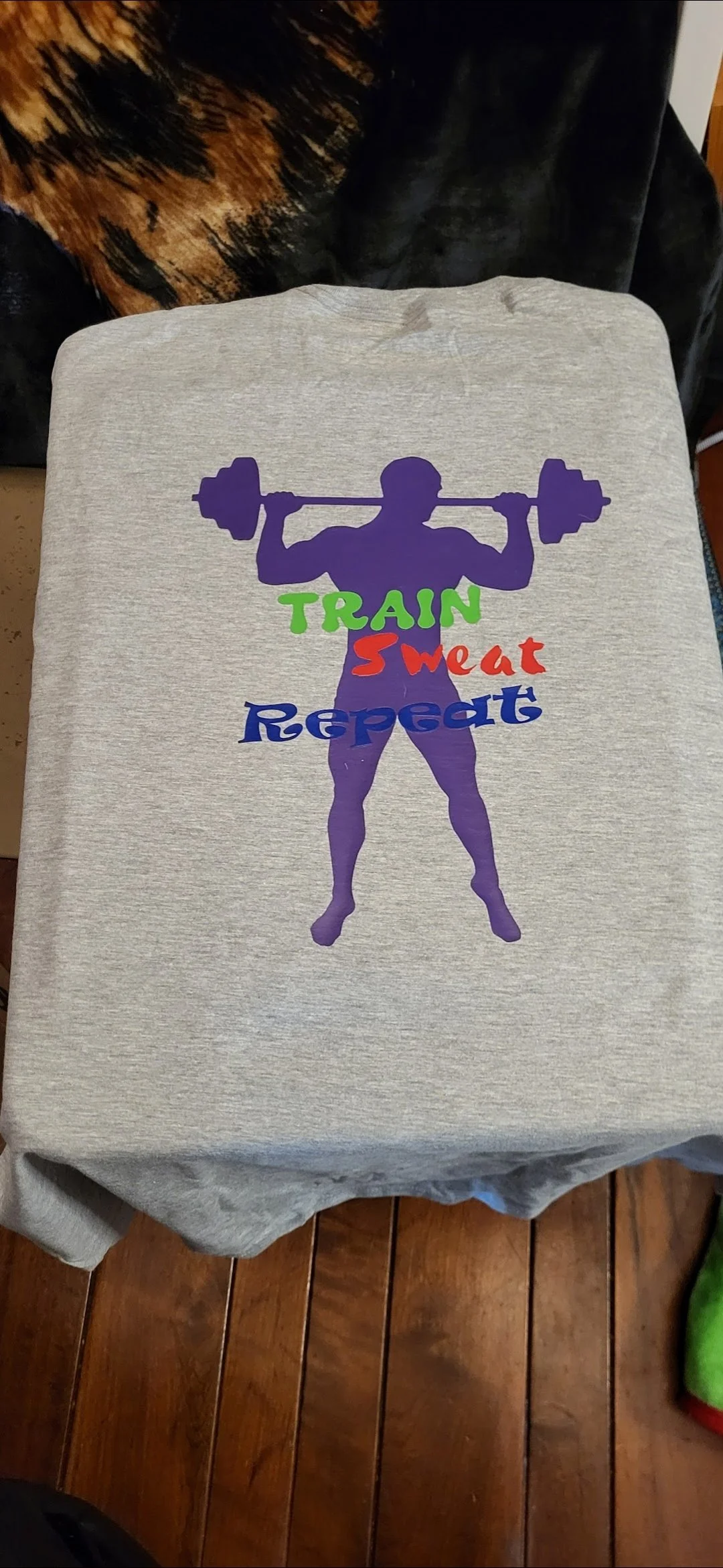 Gray sweatshirt with a graphic of a muscular person lifting a barbell, and the words 'Train Sweat Repeat' in colorful fonts.