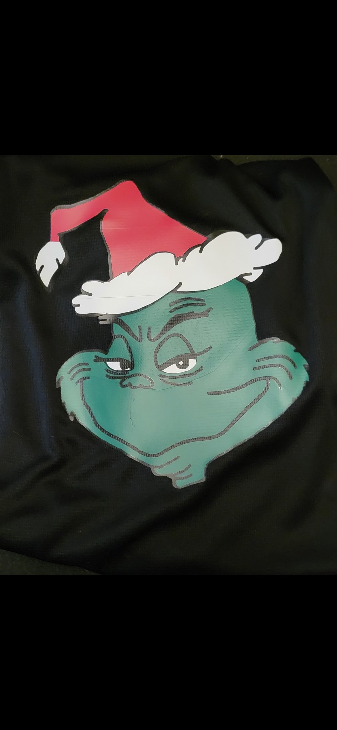 A black fabric featuring a cartoon graphic of the Grinch wearing a Santa hat, with a mischievous expression.