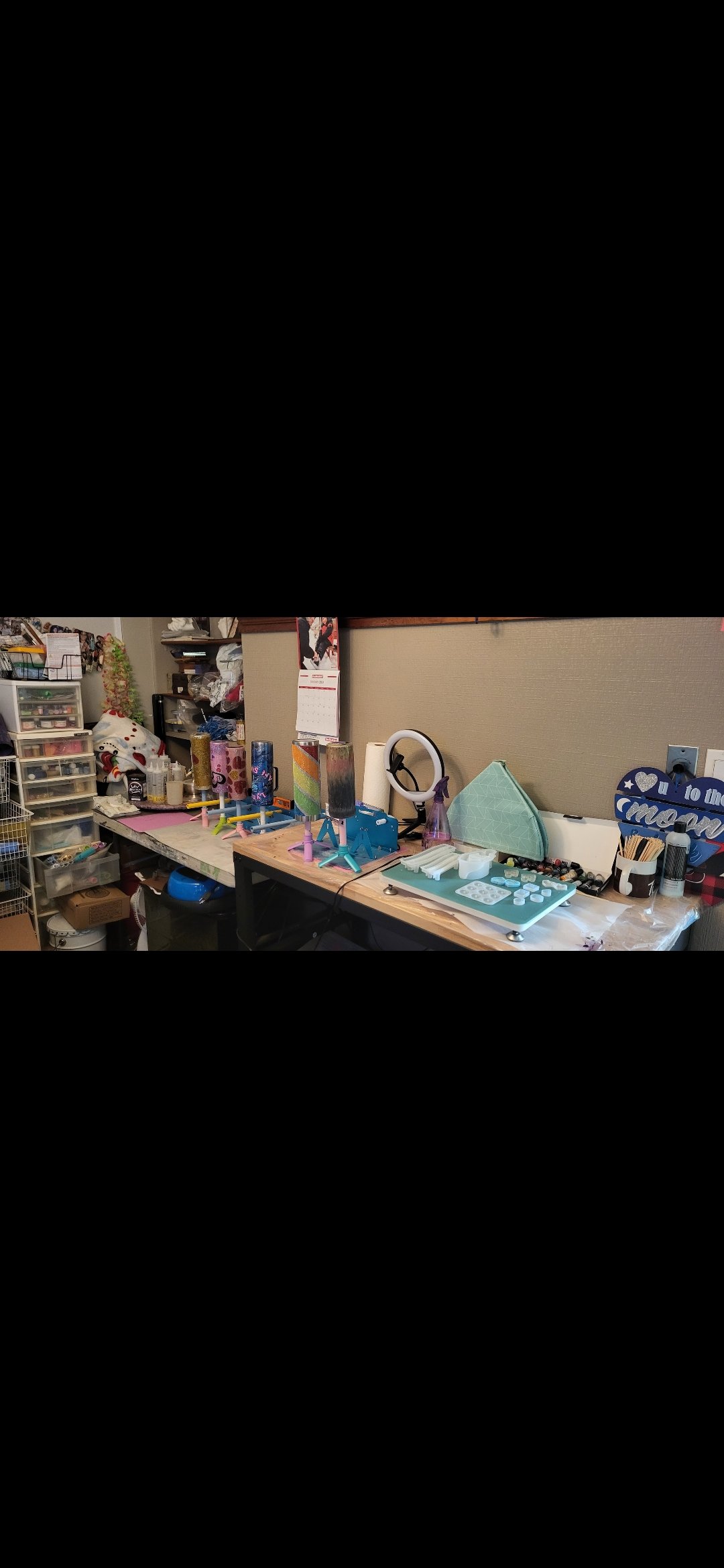Workstation with rotating cylindrical objects on stands, craft supplies, and tools, in a cluttered craft room.