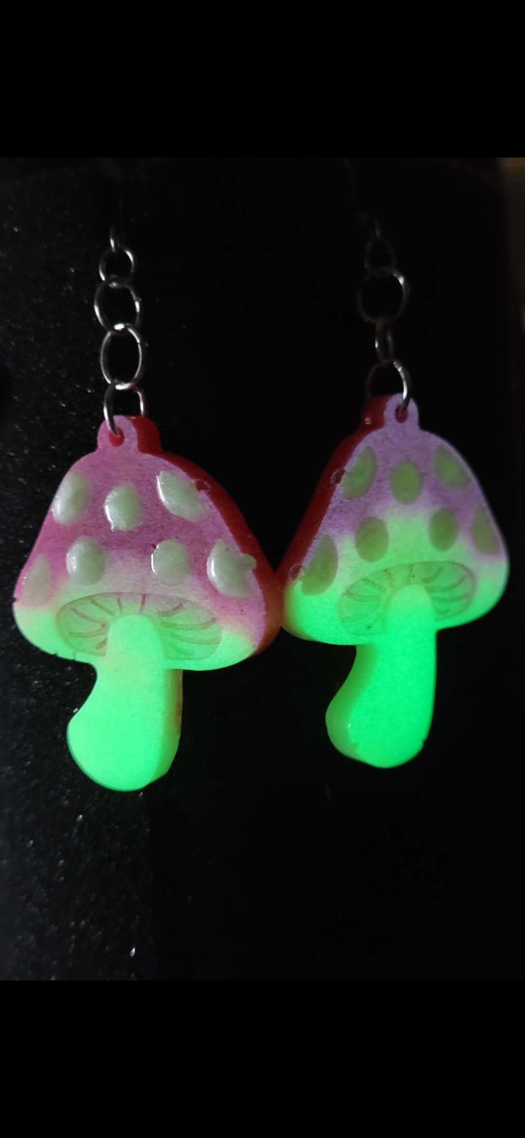 Glow-in-the-dark mushroom-shaped earrings with pink caps, white spots, and green stems, hanging from metal chains.