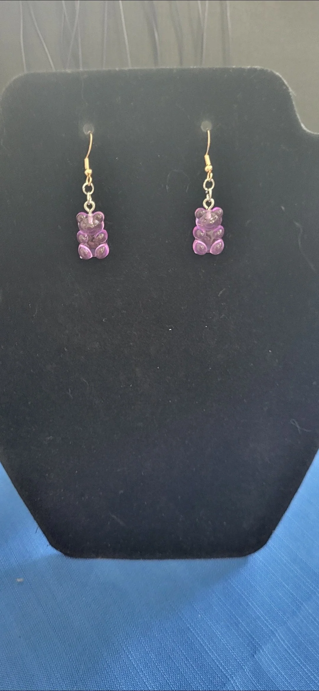 Purple teddy bear earrings on a black display stand.
