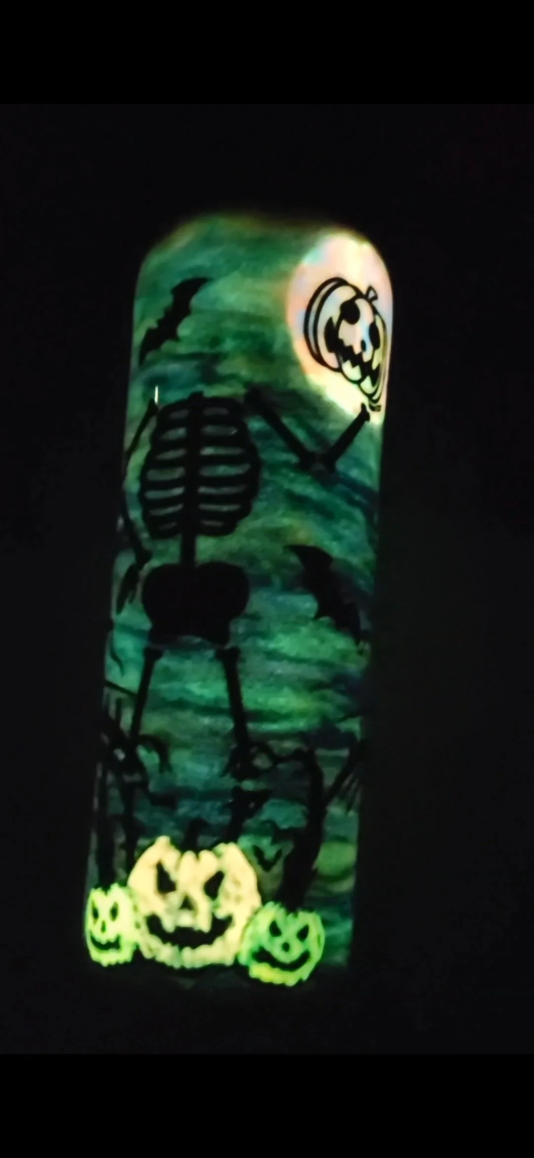 Glow-in-the-dark Halloween-themed decoration featuring a skeleton with a skull face, pumpkins, and bats against a dark background.