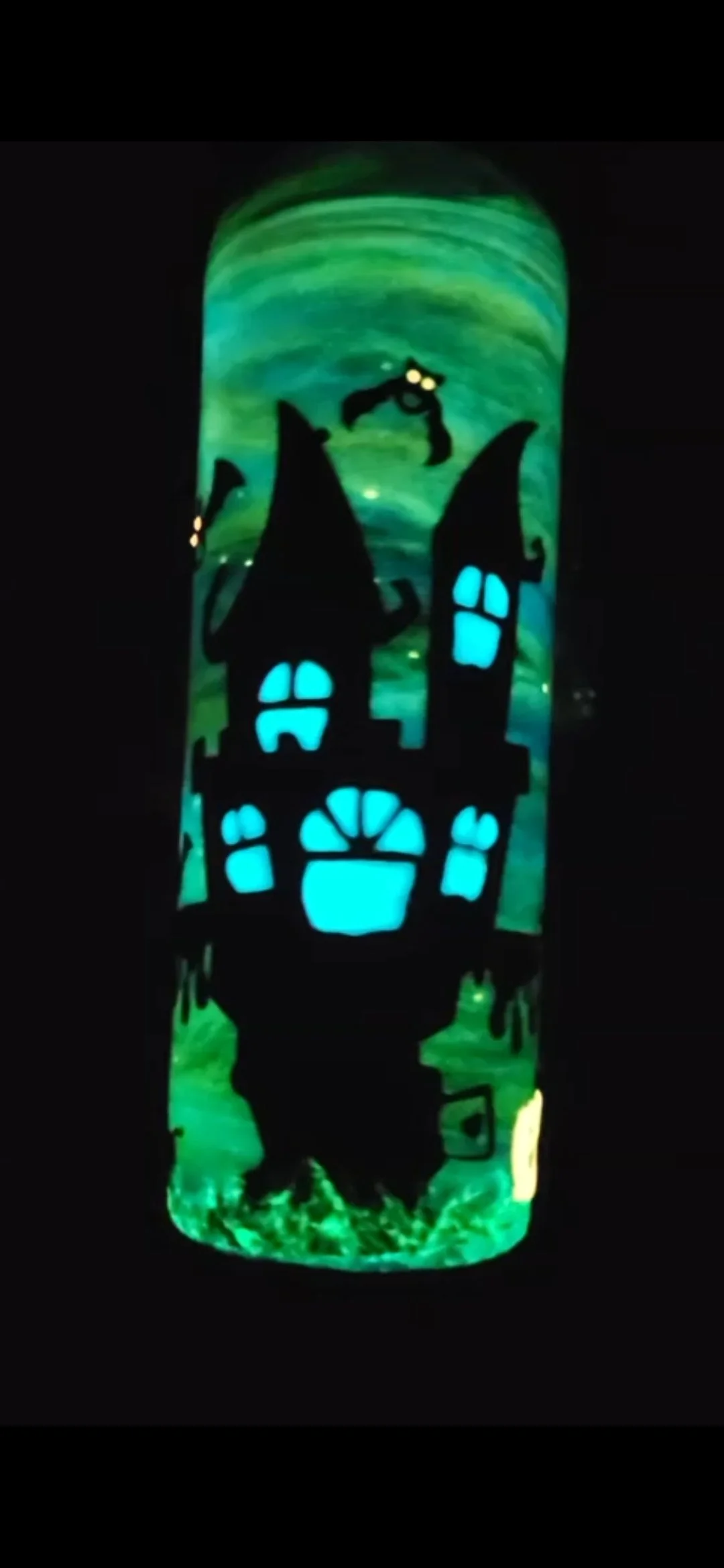 Glow-in-the-dark Halloween decoration featuring a haunted house with glowing blue windows, surrounded by green swirling background, and black bats flying above.