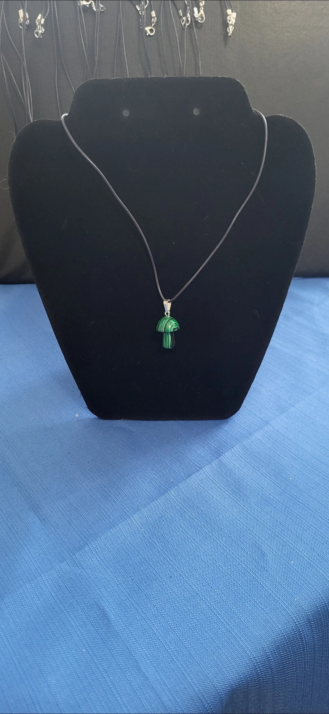 A necklace with a green mushroom pendant on a black display stand.