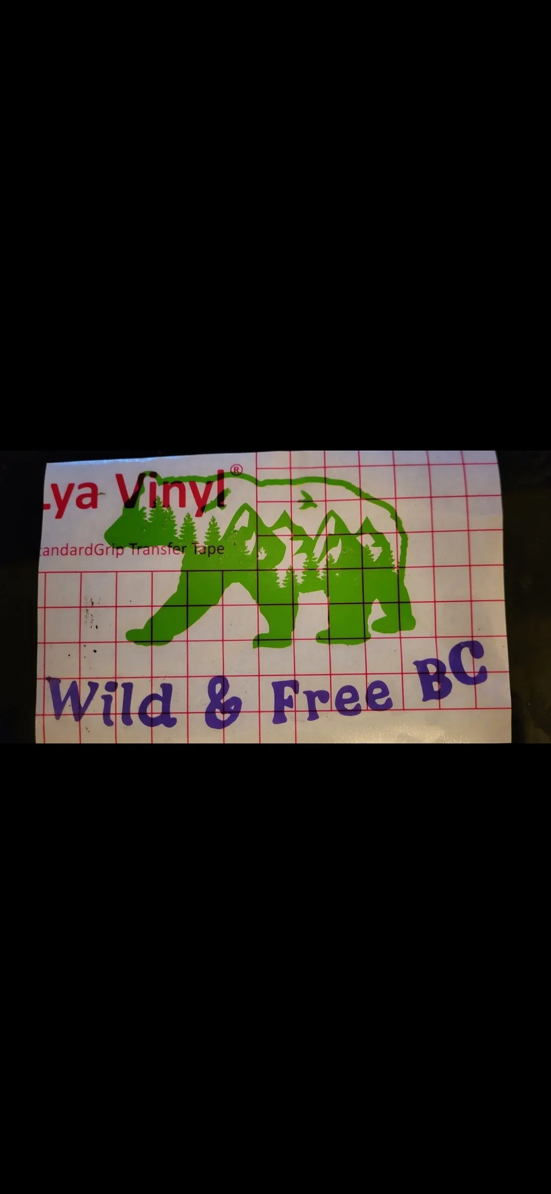 A piece of transfer tape with a green bear and tree design, partially covering red and purple printed text.