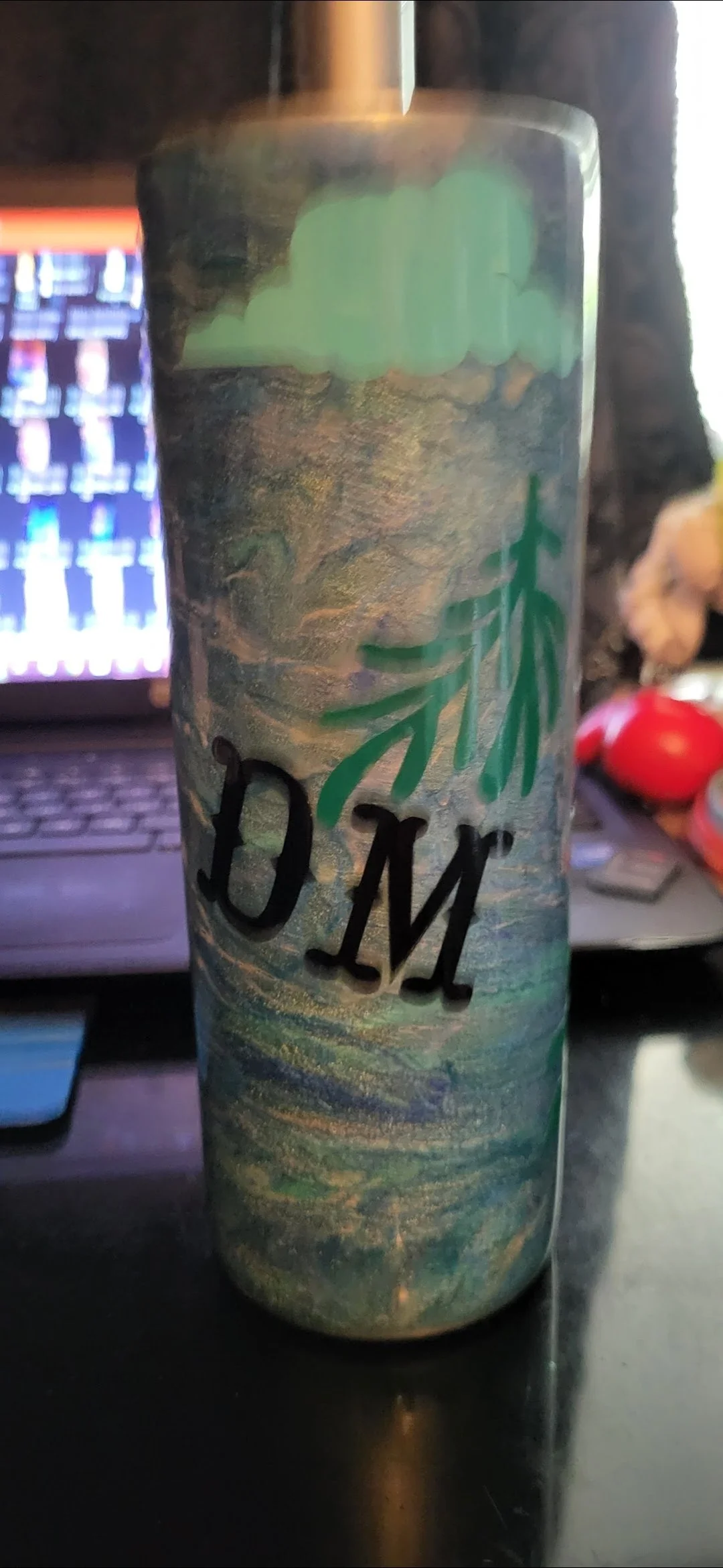 A tall cylindrical container decorated with a nature-themed design, featuring a face with closed eyes, greenery, and the word 'MOM' written in bold black letters.
