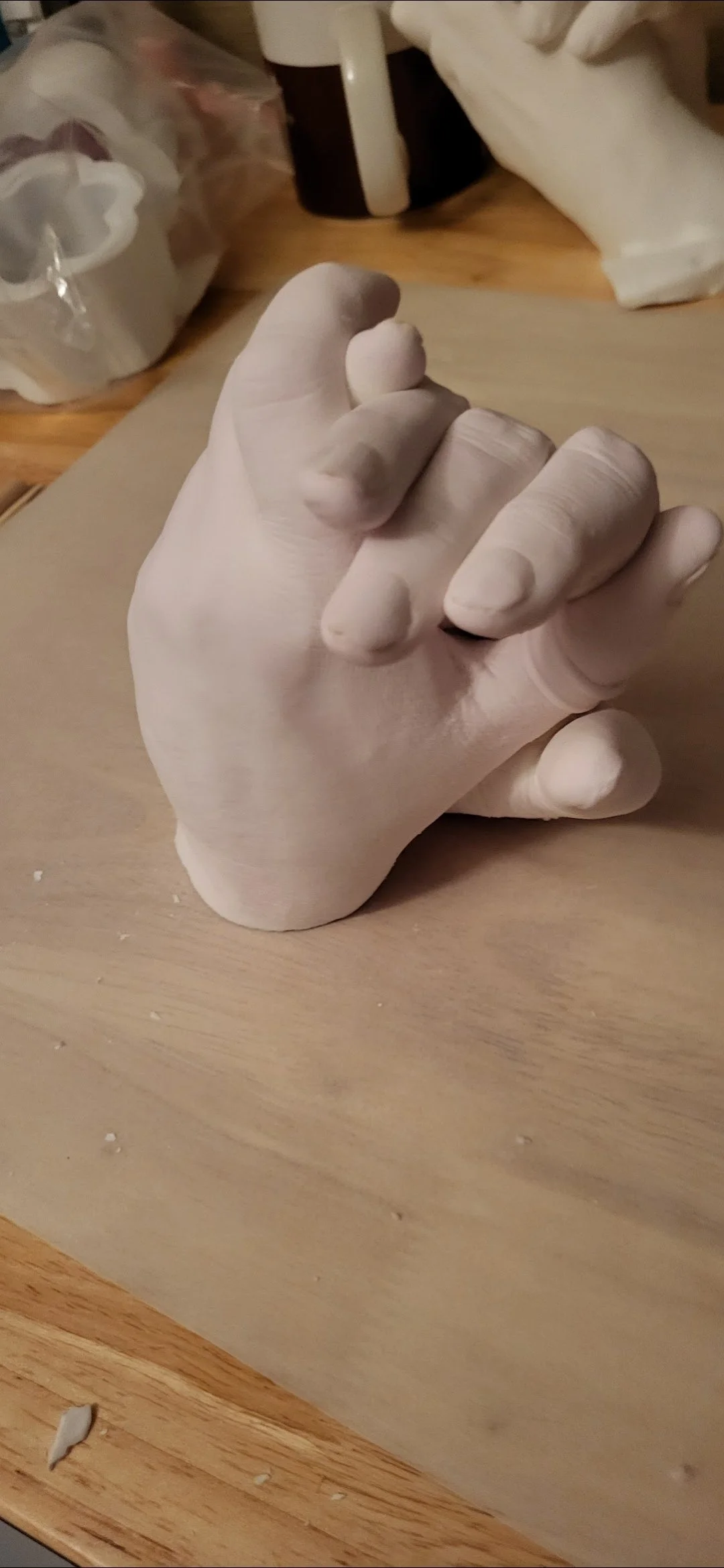 Clay sculpture of a hand resting on a wooden table, with crafting tools and supplies in the background.