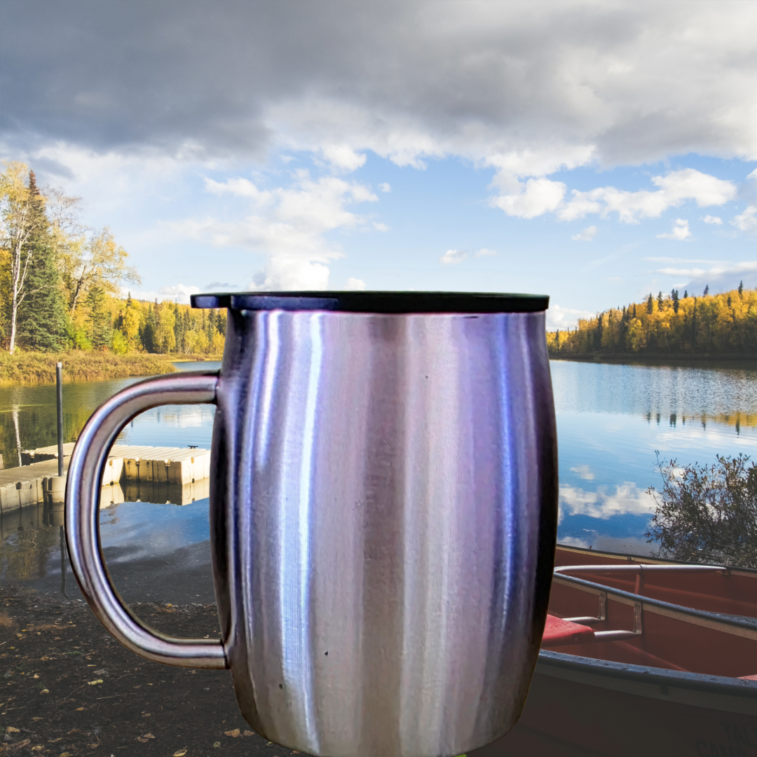 Stainless steel travel mug with black lid in front of a lake with trees and boat in the background, under cloudy sky.