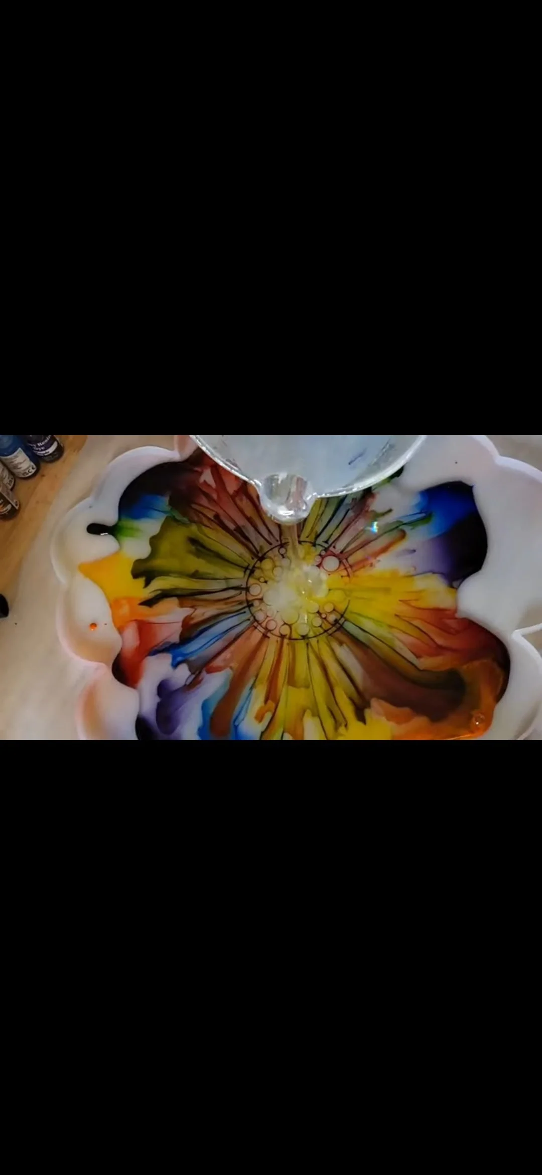 Colorful liquid art swirling in a flower-shaped tray as water is poured into it.