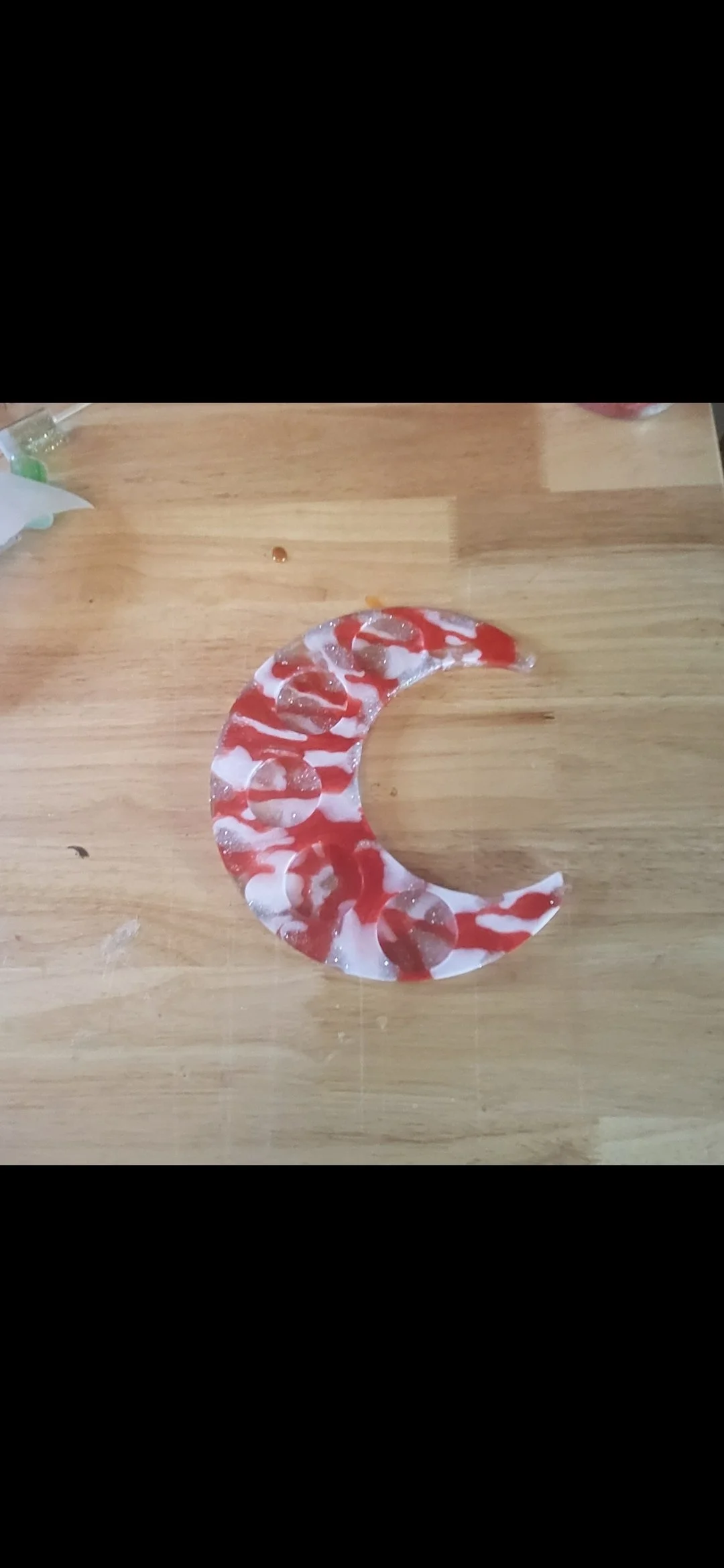 A crescent moon shape made of red and white swirled candy on a wooden surface.