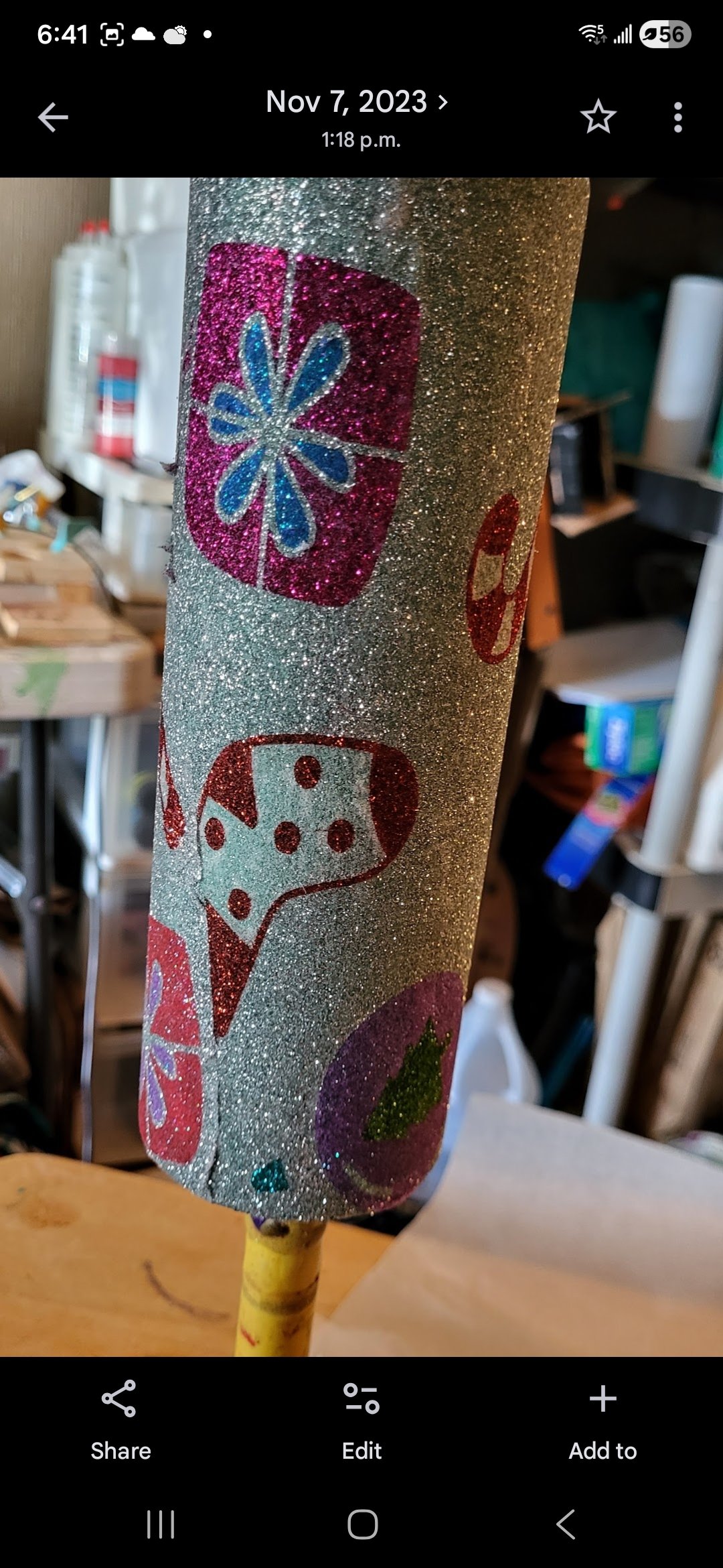 A decorated cylindrical object with silver glitter and colorful stickers, including a snowflake, a ladybug, and a Christmas ornament.