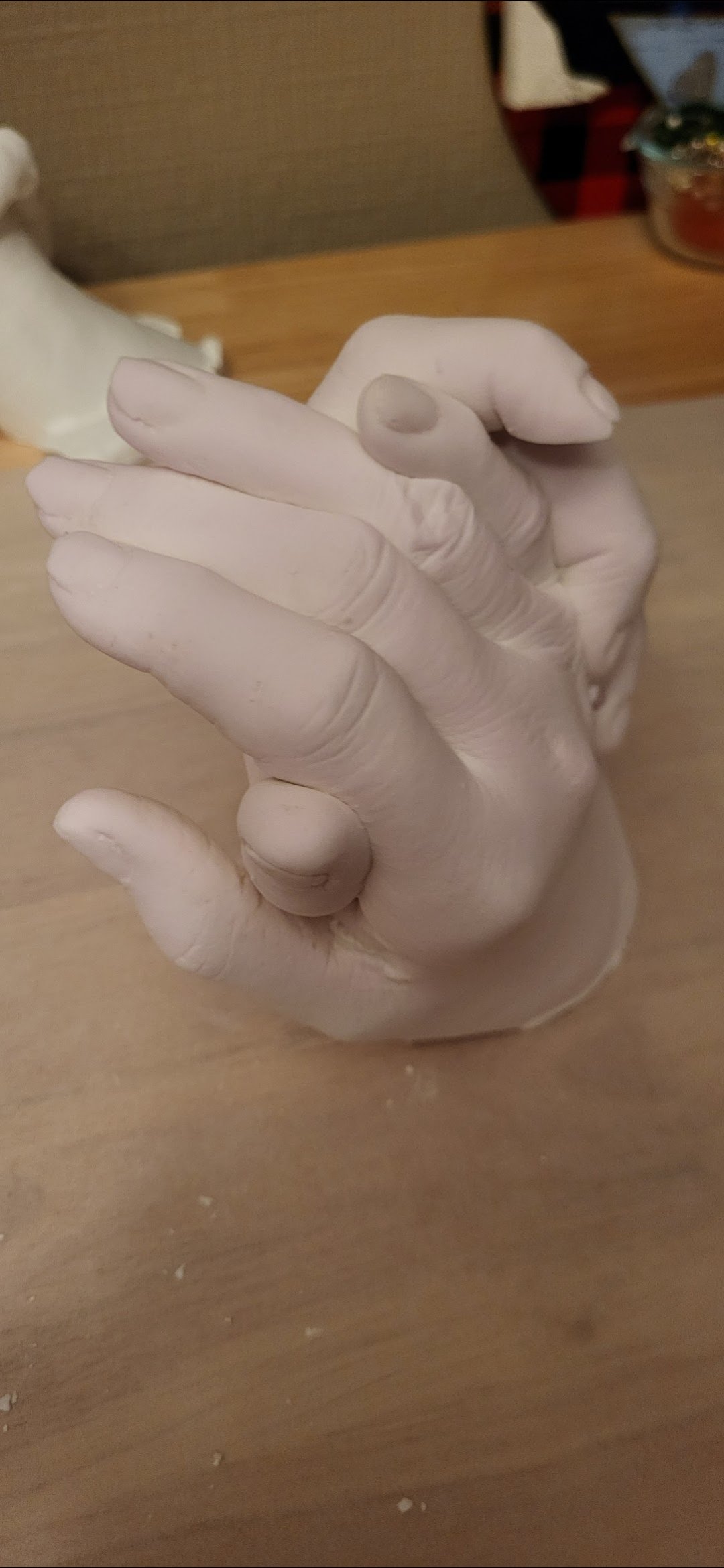 A white porcelain hand sculpture with the thumb and index finger forming an OK gesture, placed on a wooden surface.