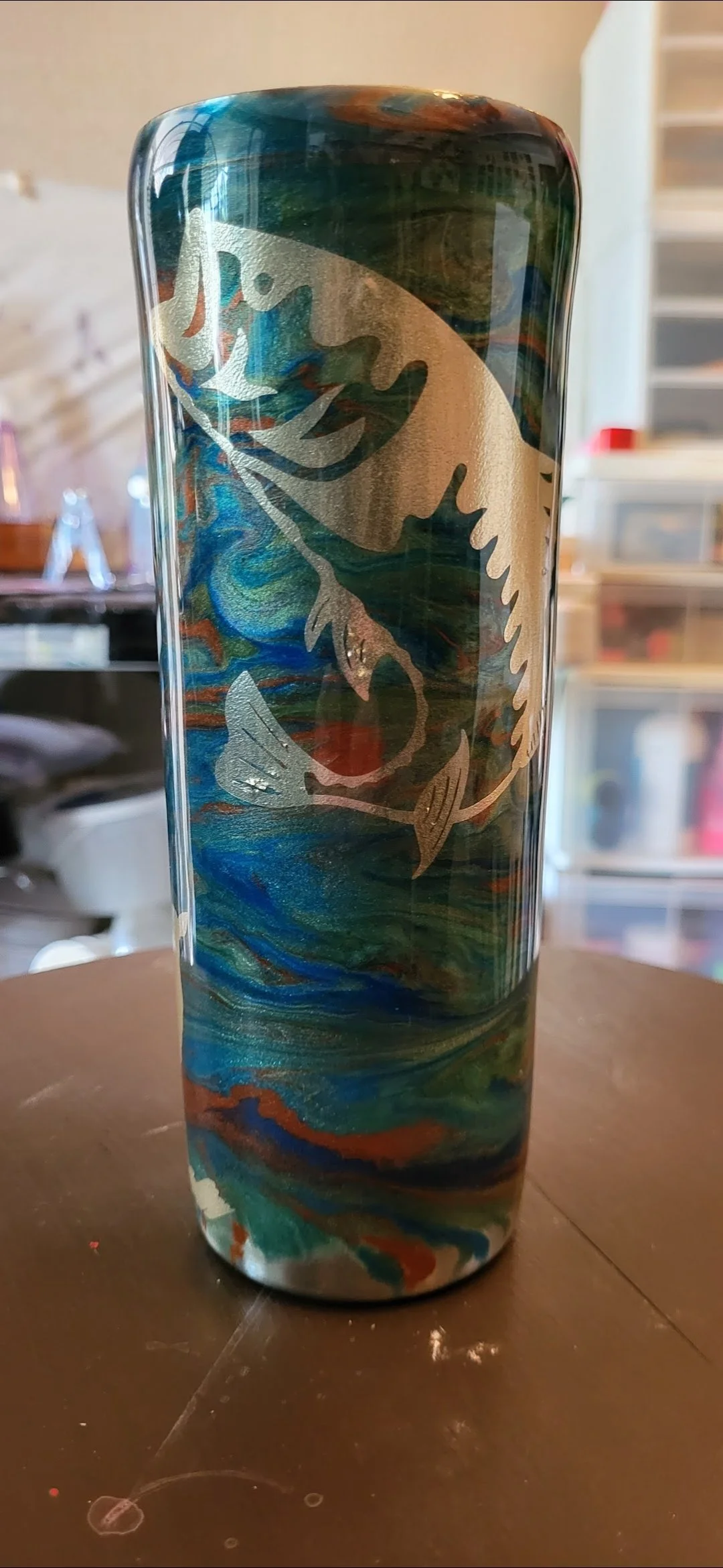 A tall, cylindrical tumbler with a swirling, marbled pattern in blue, green, black, and orange. It features a metallic or foil dragon design wrapping around the surface.