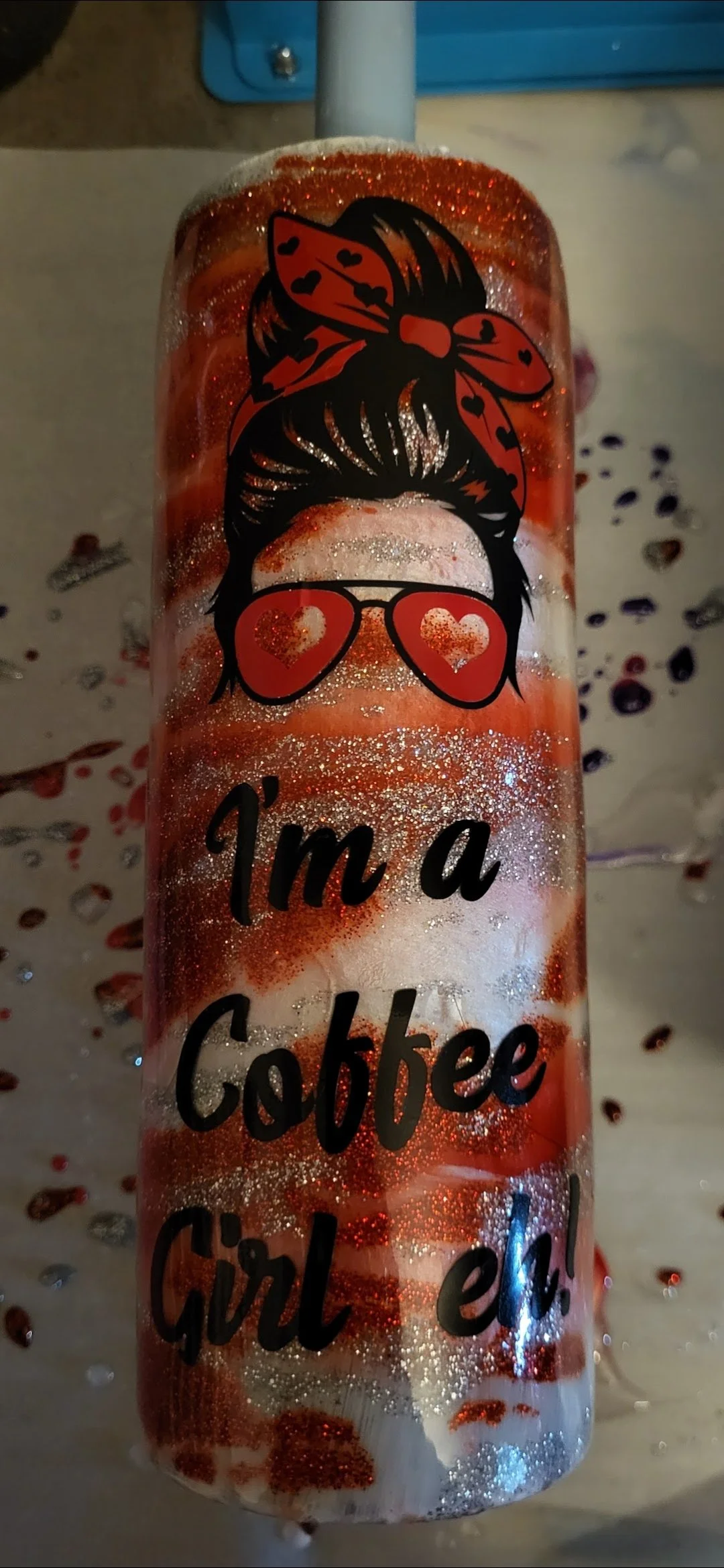 A glittery tumbler with a design of a woman's hairstyle with a big bow and hair in a bun, wearing heart-shaped sunglasses. Text on the tumbler reads, "I'm a Cobbee Girl!" surrounded by scattered heart-shaped confetti.