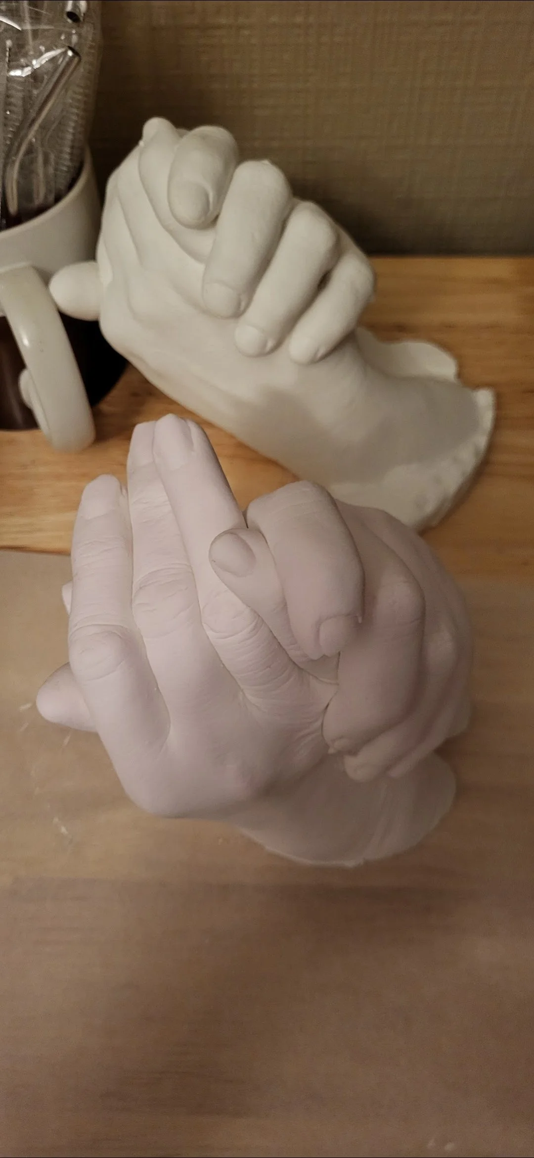 Two ceramic hand sculptures holding each other on a wooden surface.