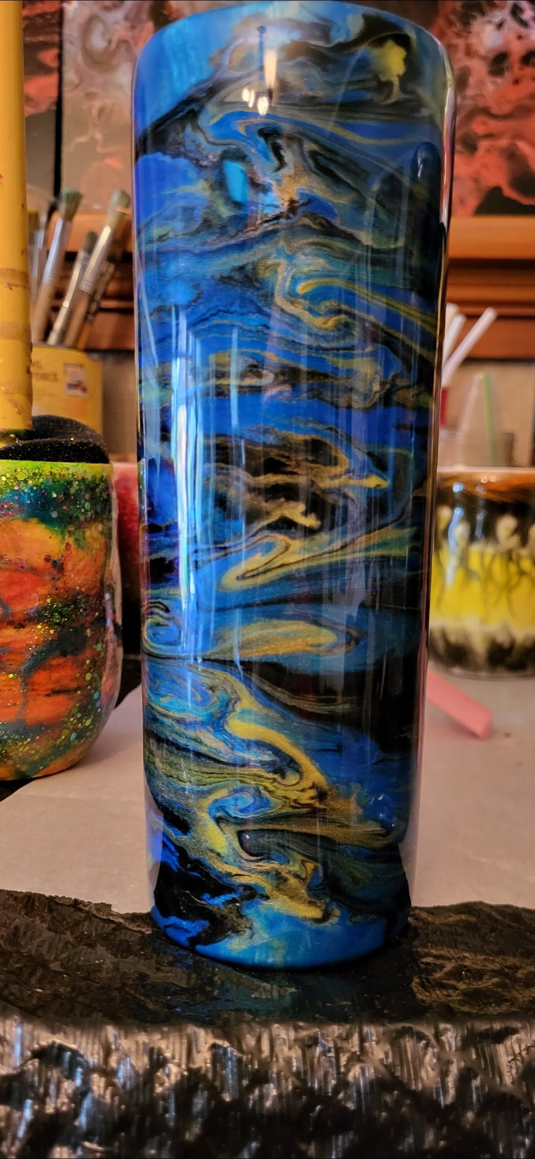 A colorful glass art piece with blue, yellow, black, and white swirls, placed on a workbench in an art studio.