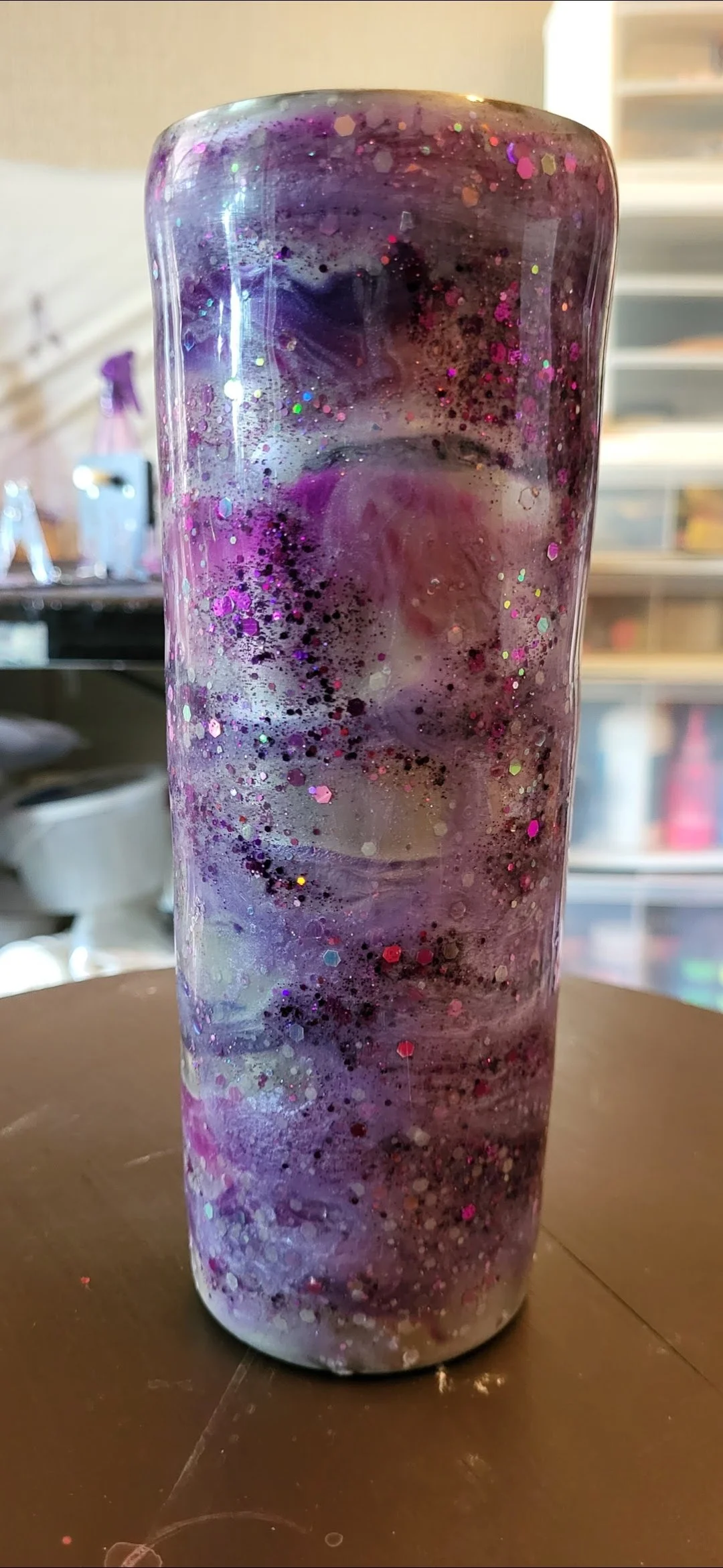 A tall, cylindrical object with a marbled purple, pink, and white pattern, decorated with glitter and sparkles.