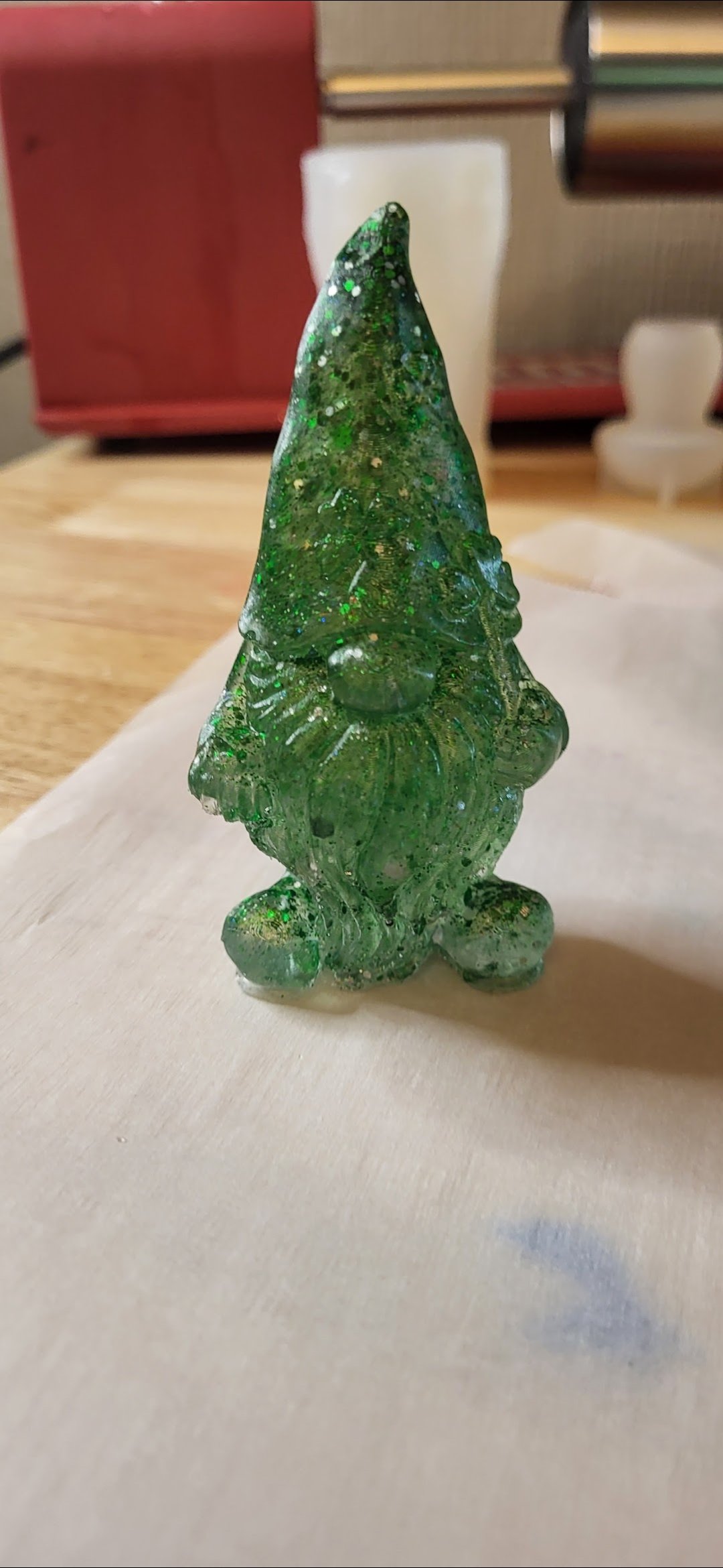 Green glass figurine shaped like a gnome with a pointed hat, large nose, and beard, sitting on a wooden surface.