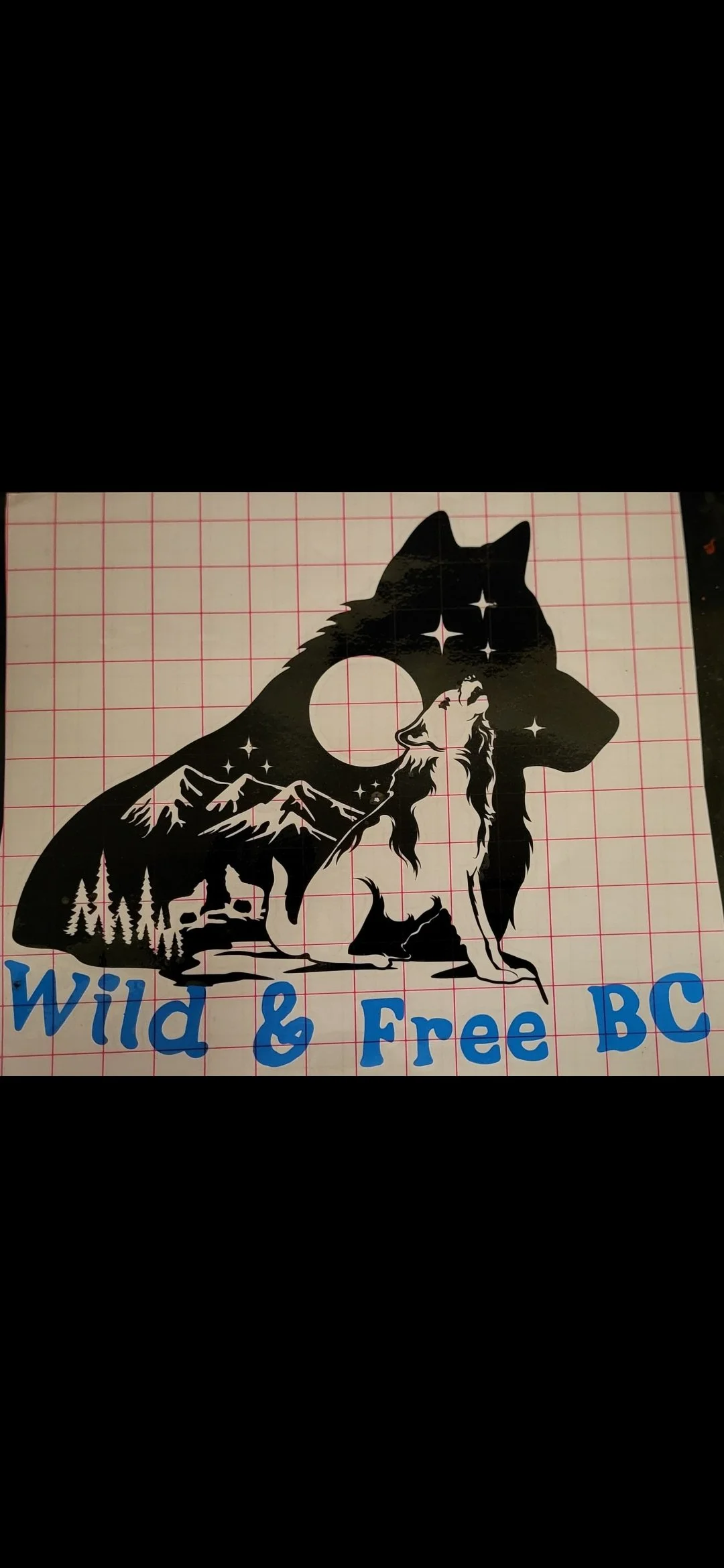 A black and white sticker of a wolf silhouette with a landscape scene inside, including mountains, trees, a full moon, and stars. Below the wolf, blue text reads "Wild & Free BC."