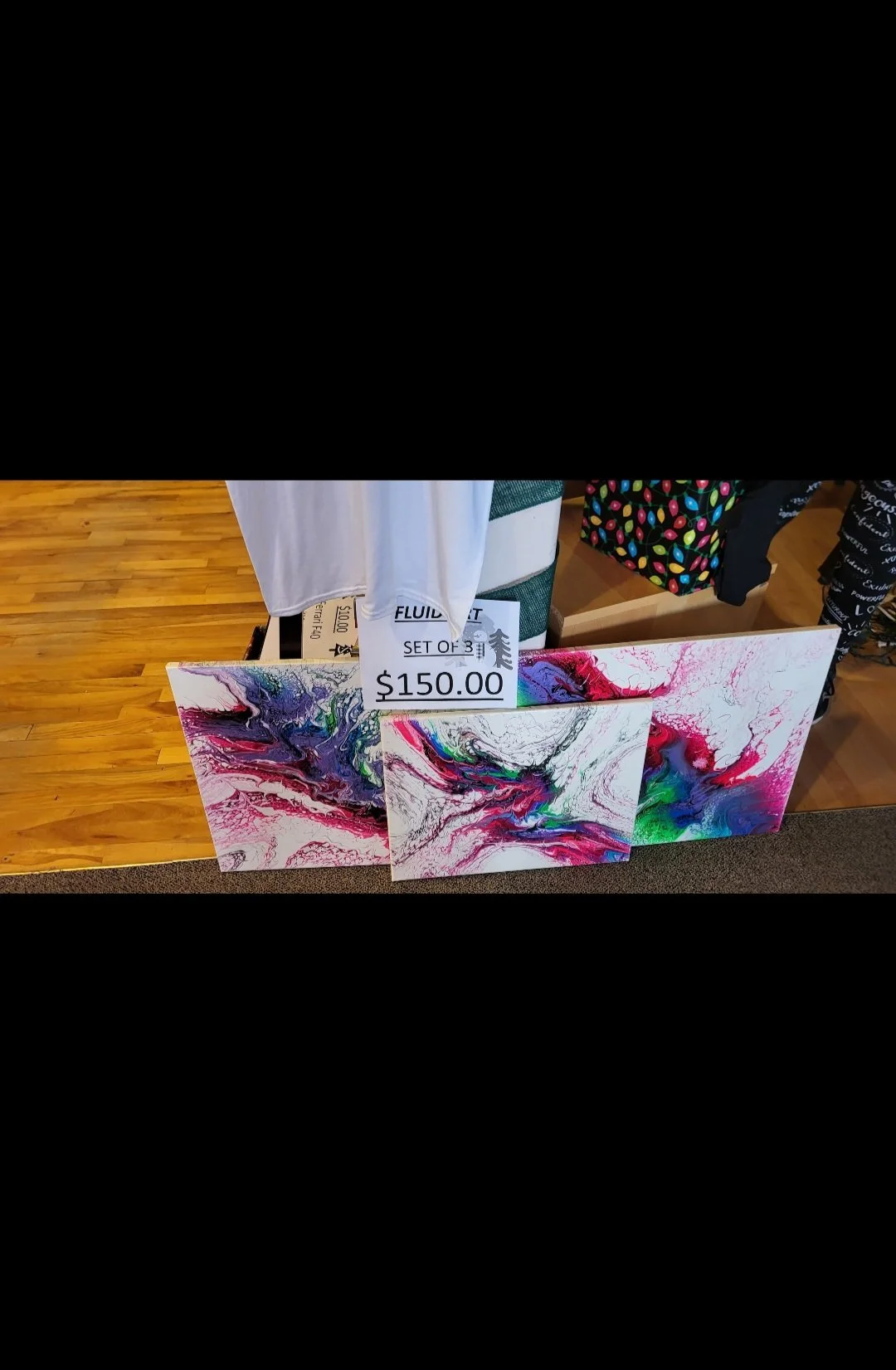 Set of three abstract paintings with colorful swirling patterns, displayed on a table with a price tag of $150.00.