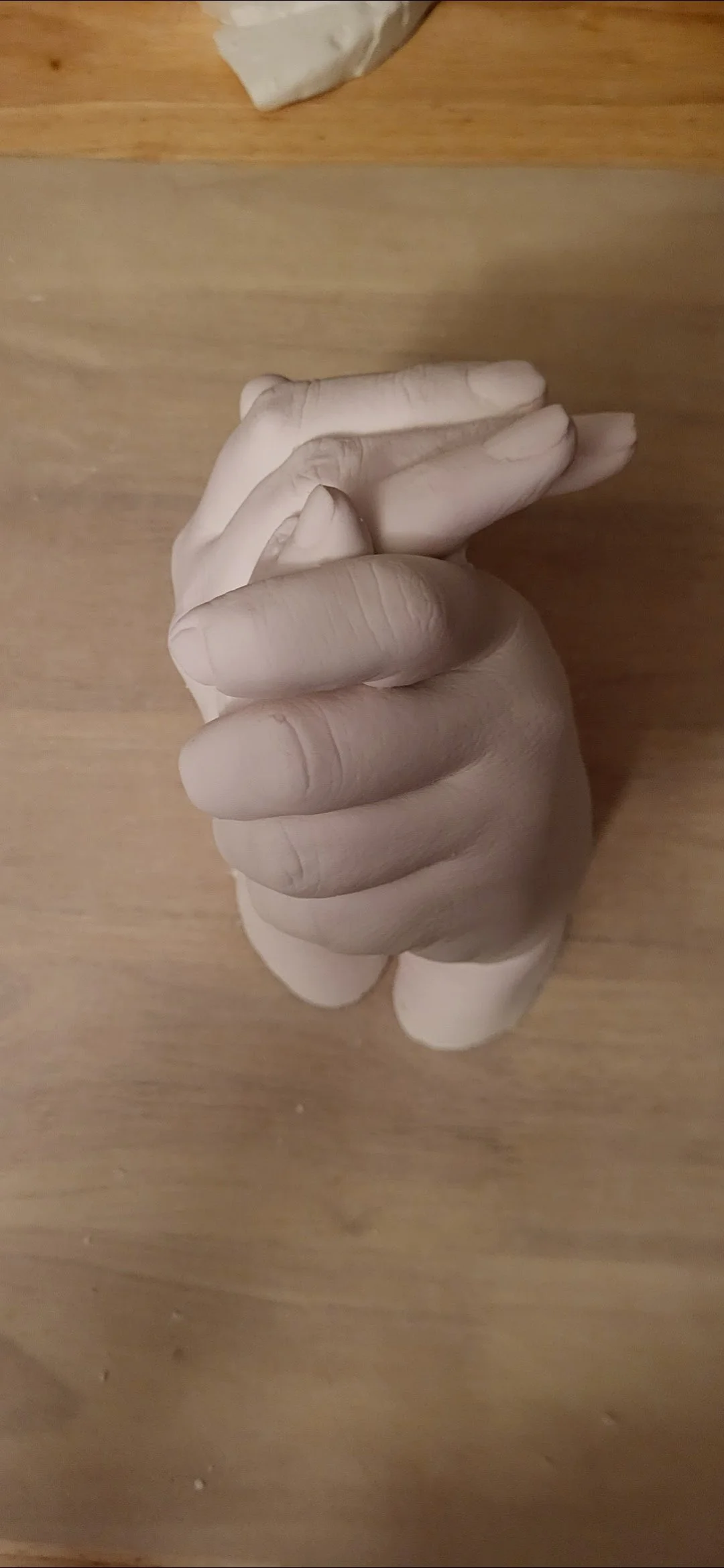 A detailed view of a white sculpture of a human hand with fingers intertwined, placed on a wooden surface.
