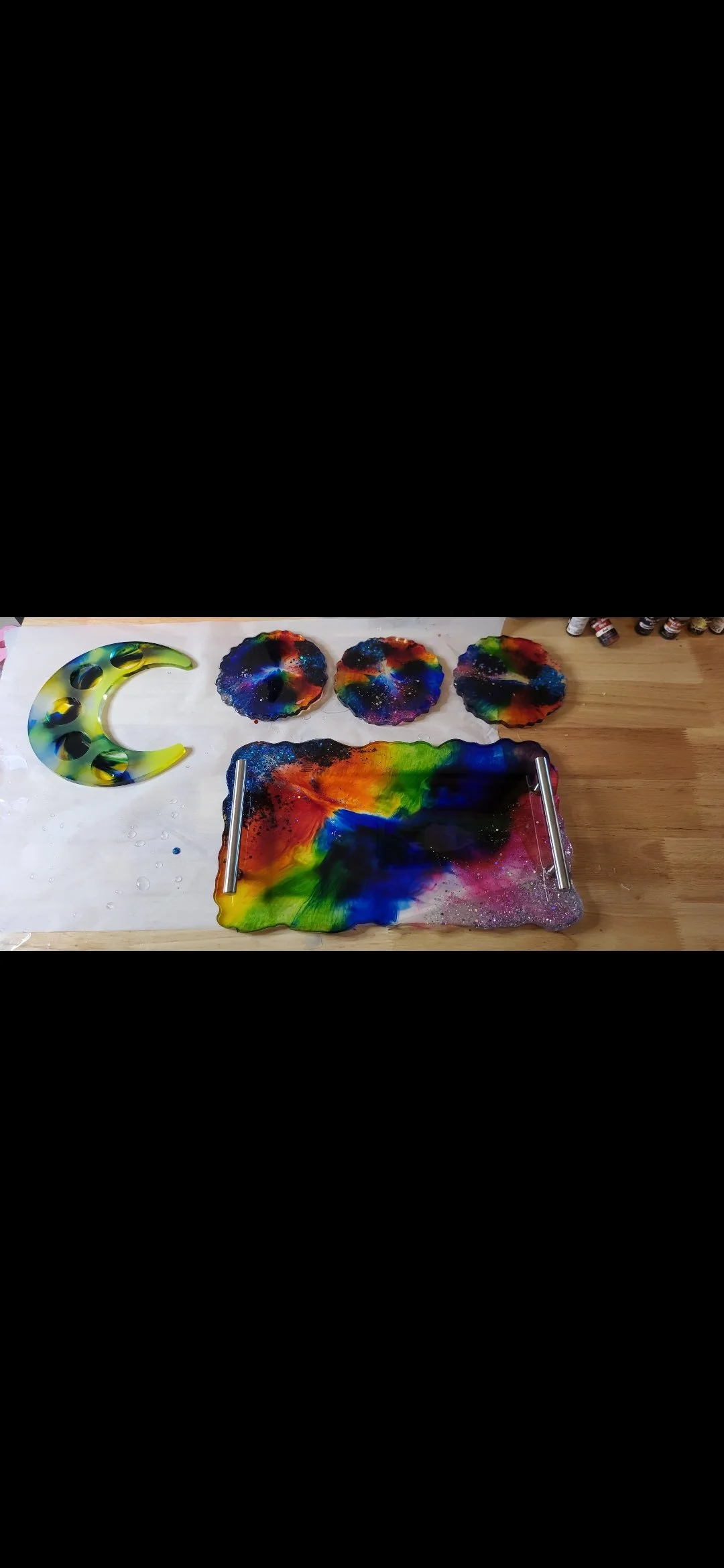 Colorful, abstract glass art with a crescent moon shape and three circular pieces on a wooden surface.