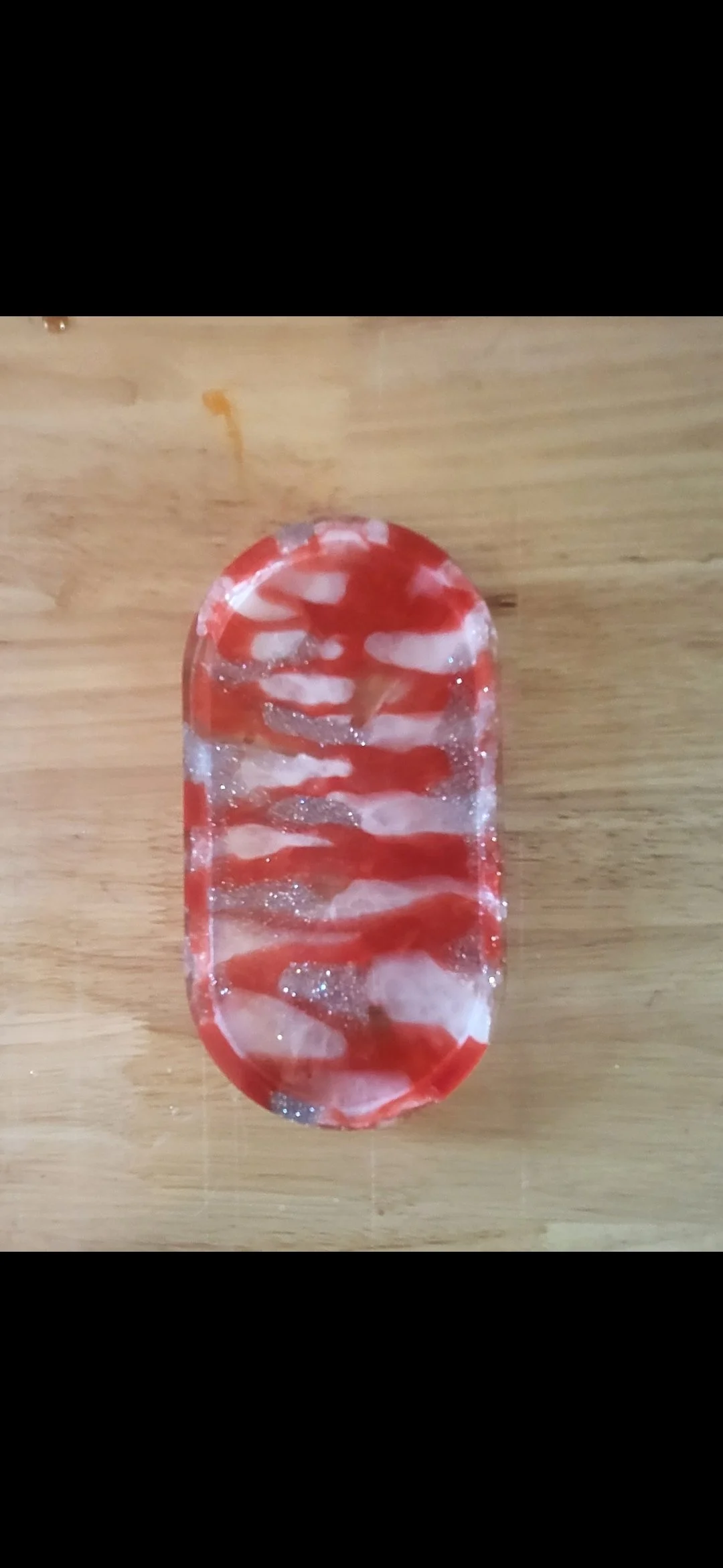 A soap with red and white swirled pattern and glitter detail on a wooden surface.