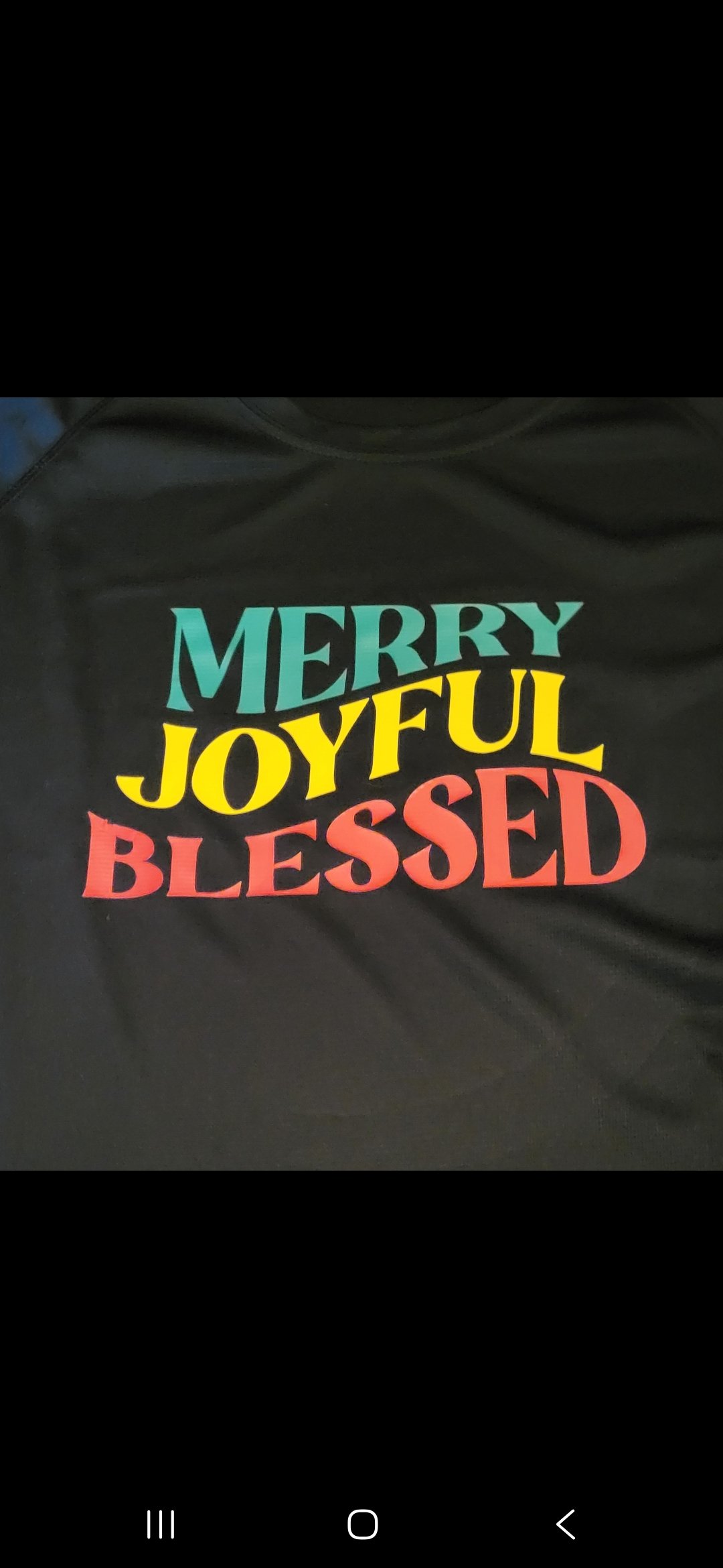 A black fabric item with the words 'MERRY JOYFUL BLESSED' printed in colorful, bold letters.