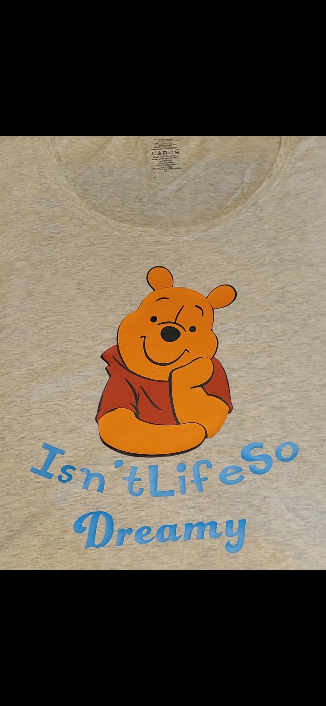 A beige T-shirt featuring Winnie the Pooh with a thought expression and the text "I isn't so Dreamy" in blue letters.