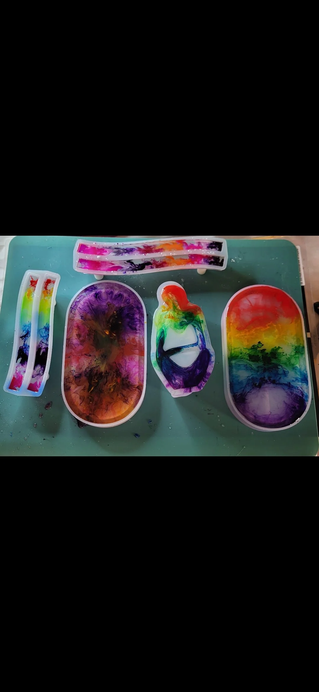 Colorful, abstract swirling paint art in various trays and containers on a green surface.