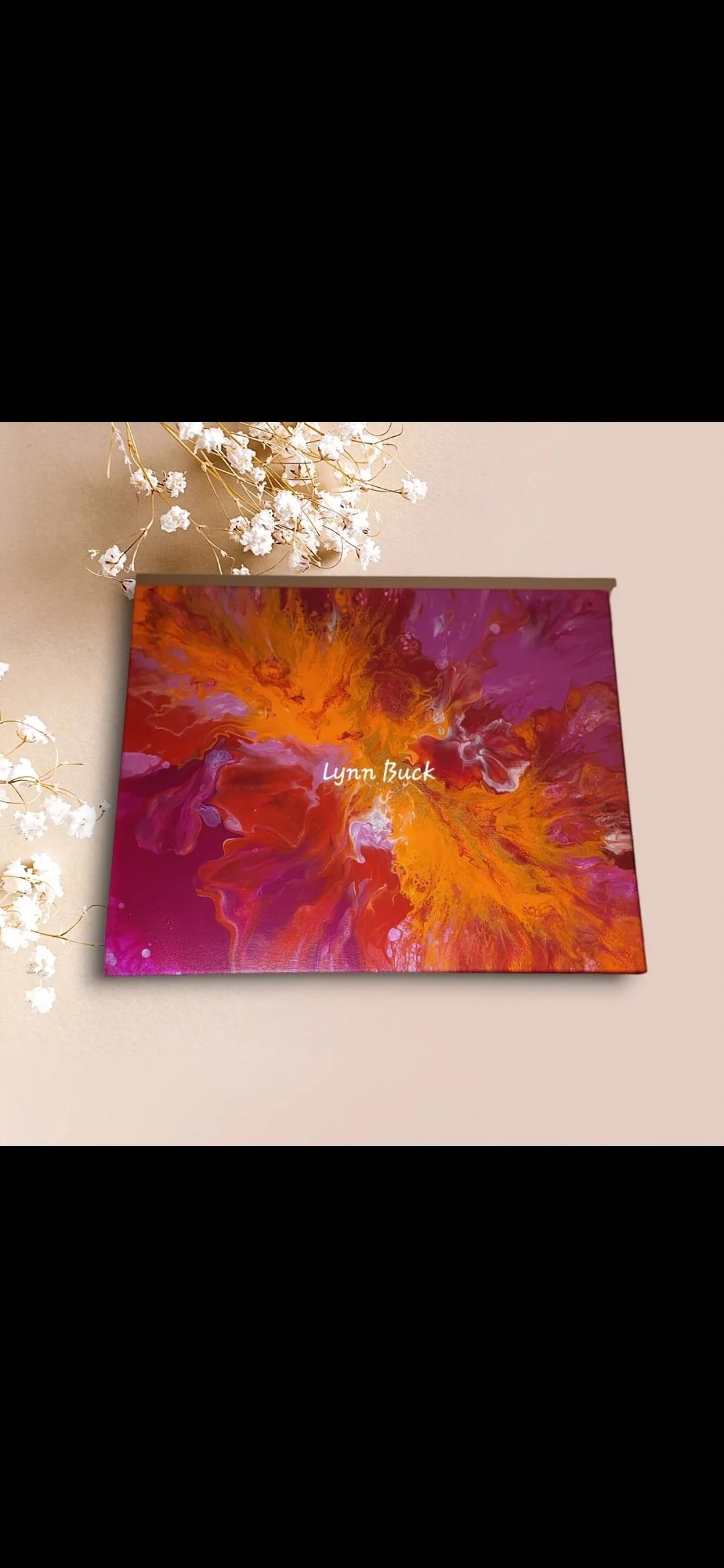 Decorative abstract painting with swirls of orange, yellow, pink, and purple, with the name "Lynn Buck" written across the center. White dried flowers on a beige wall in the background.