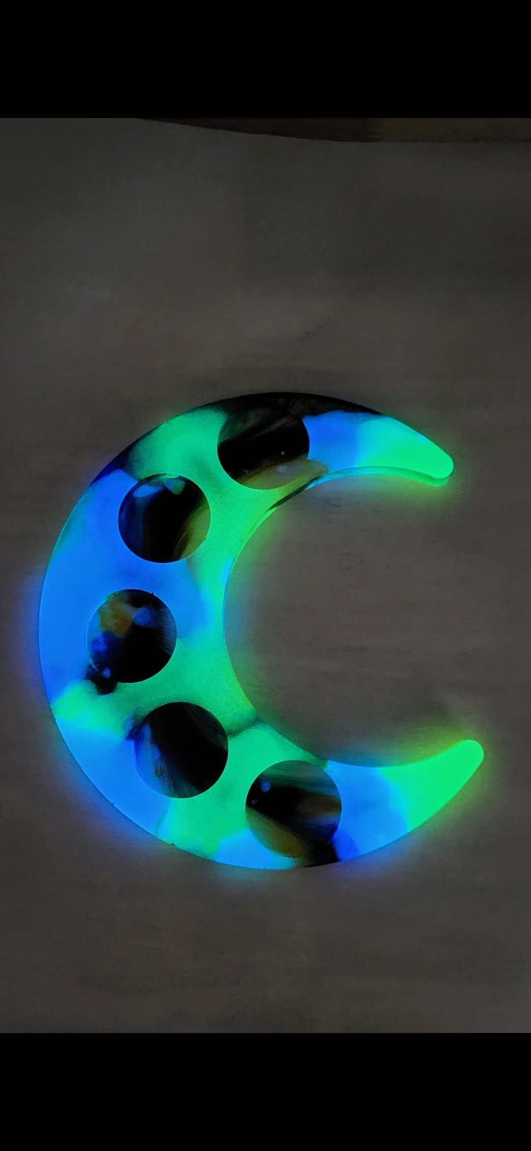 A crescent moon-shaped LED night light with black dots, emitting a glow of green and blue colors.