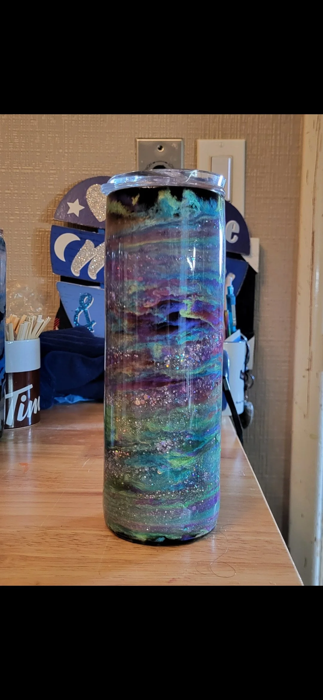 A tall cylindrical ottoman with a galaxy-inspired design featuring swirls of vibrant colors and specks resembling stars.