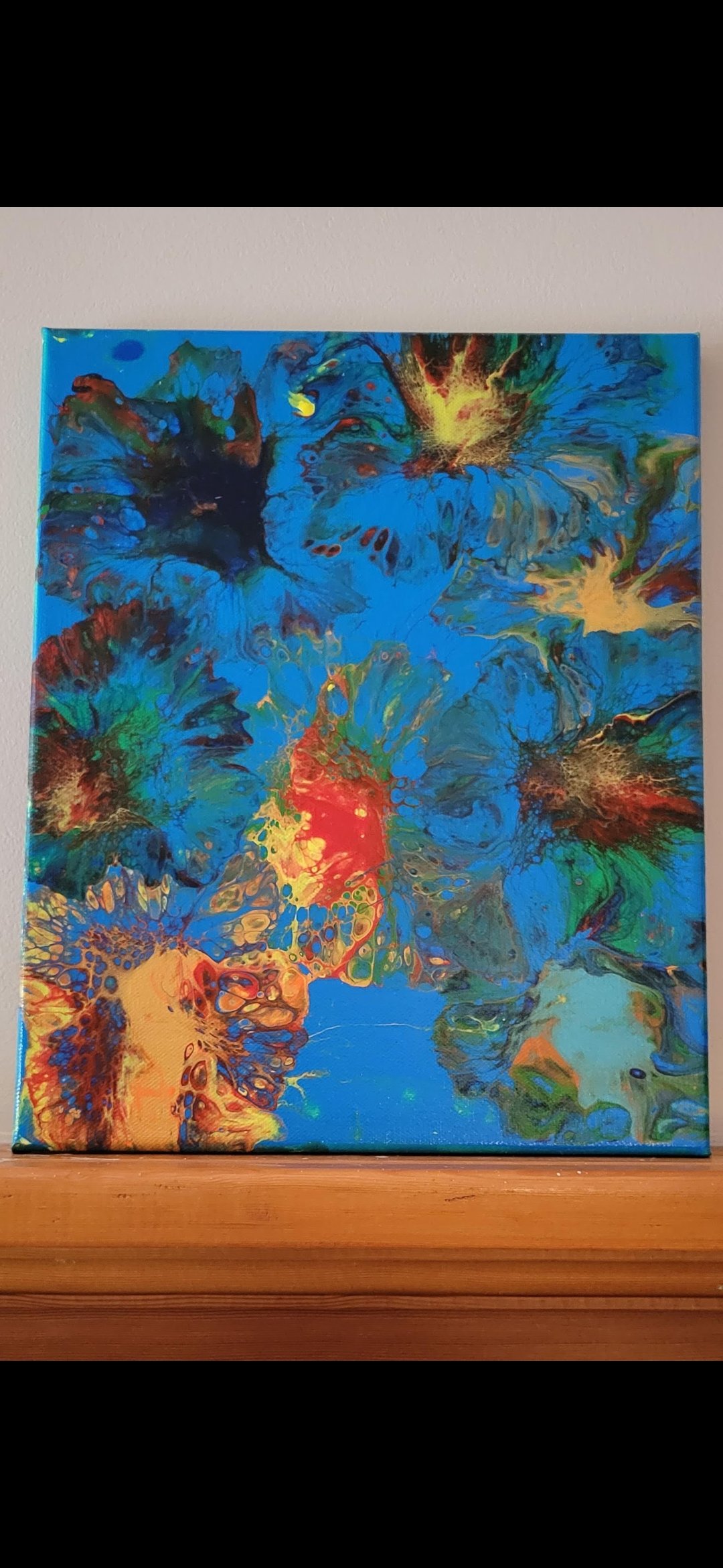 Abstract painting with blue, green, red, yellow, and orange colors on a canvas placed on a wooden surface