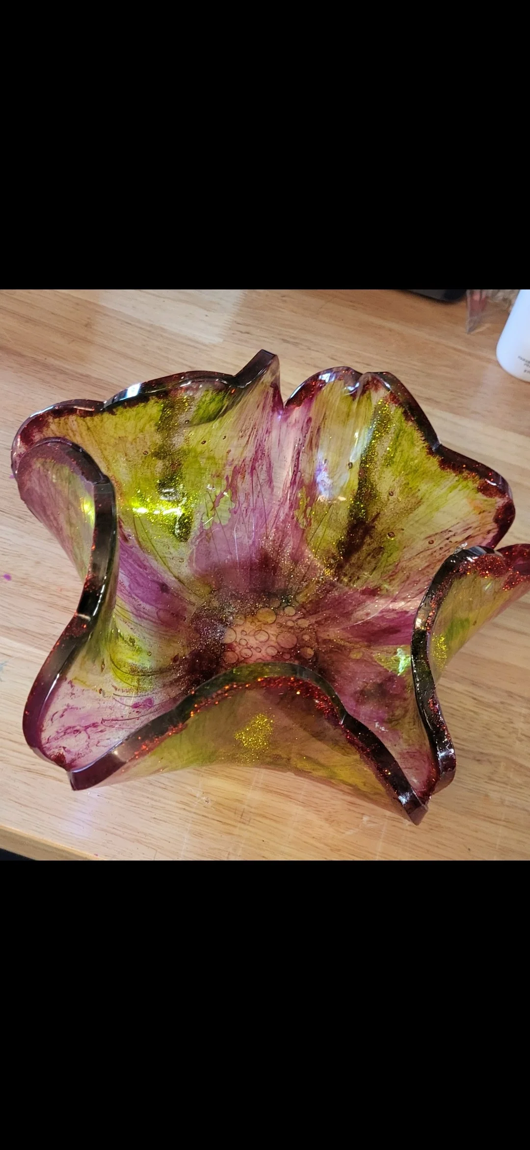 Colorful glass bowl with pink, yellow, and green hues on a wooden surface.