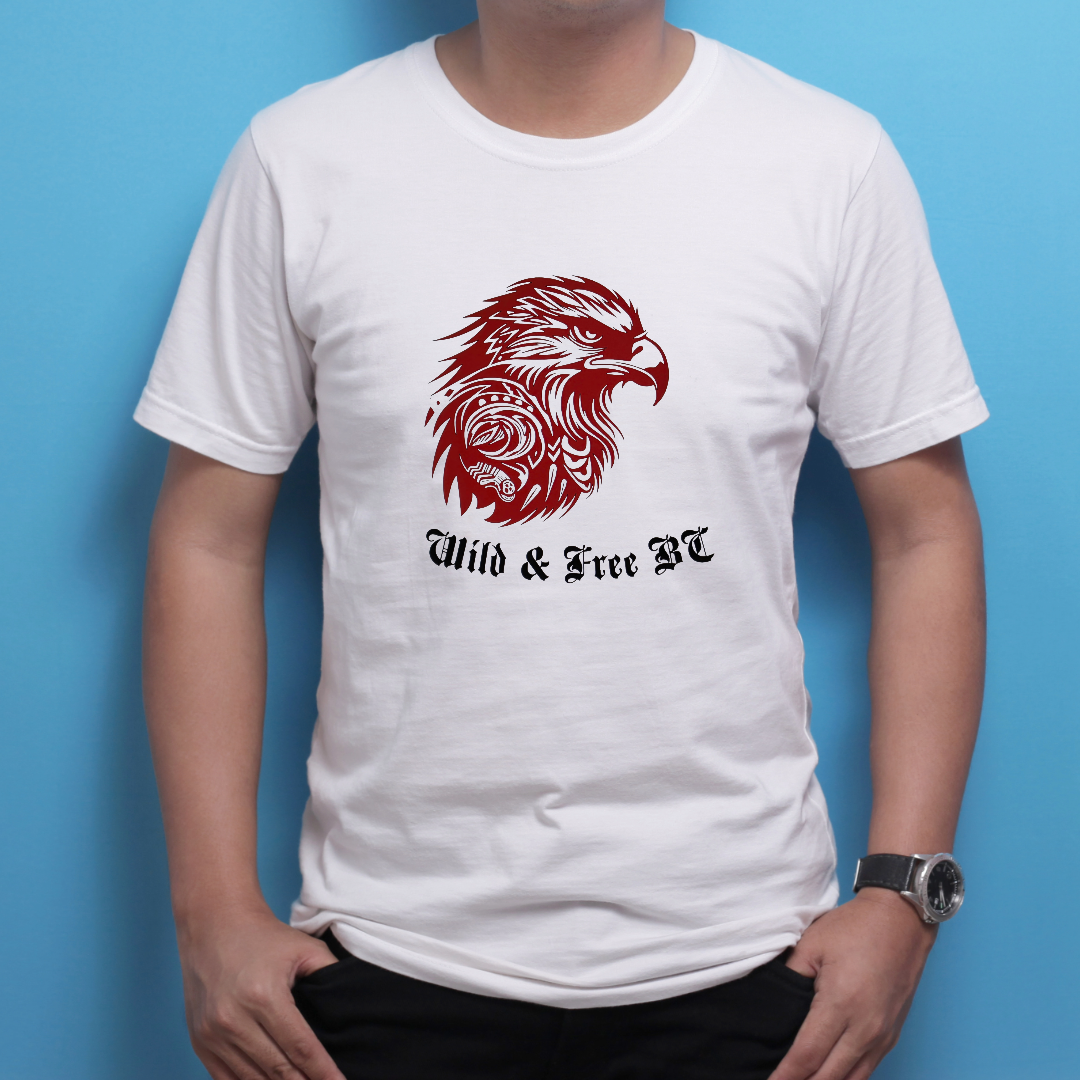 White T-shirt with a red graphic of an eagle's head and the text 'Wild & Free BC' underneath, worn by a person standing against a blue background.