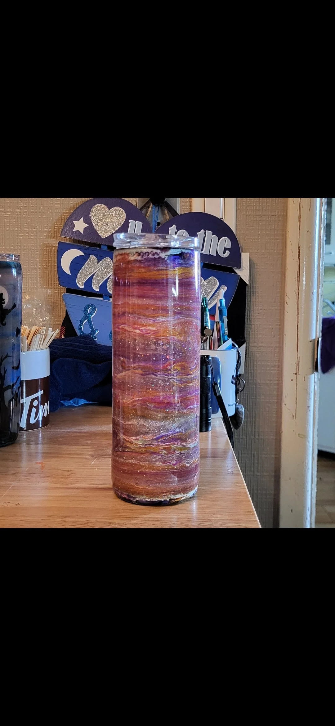 A cylindrical lava lamp with colorful swirling wax inside, placed on a wooden counter.