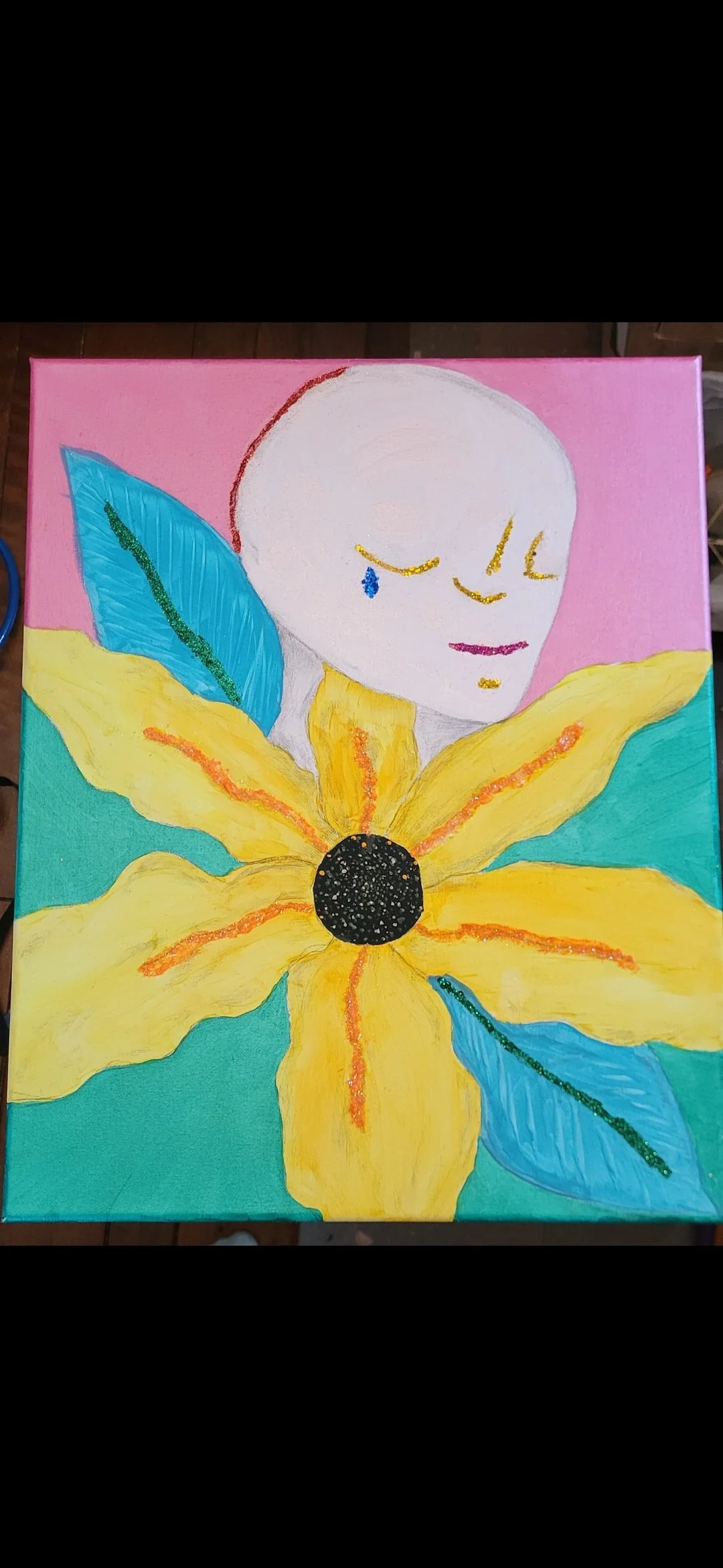 A colorful painting featuring a large yellow flower with a black center, green and blue leaves, and a human face with a neutral expression emerging from behind the flower against a pink background.