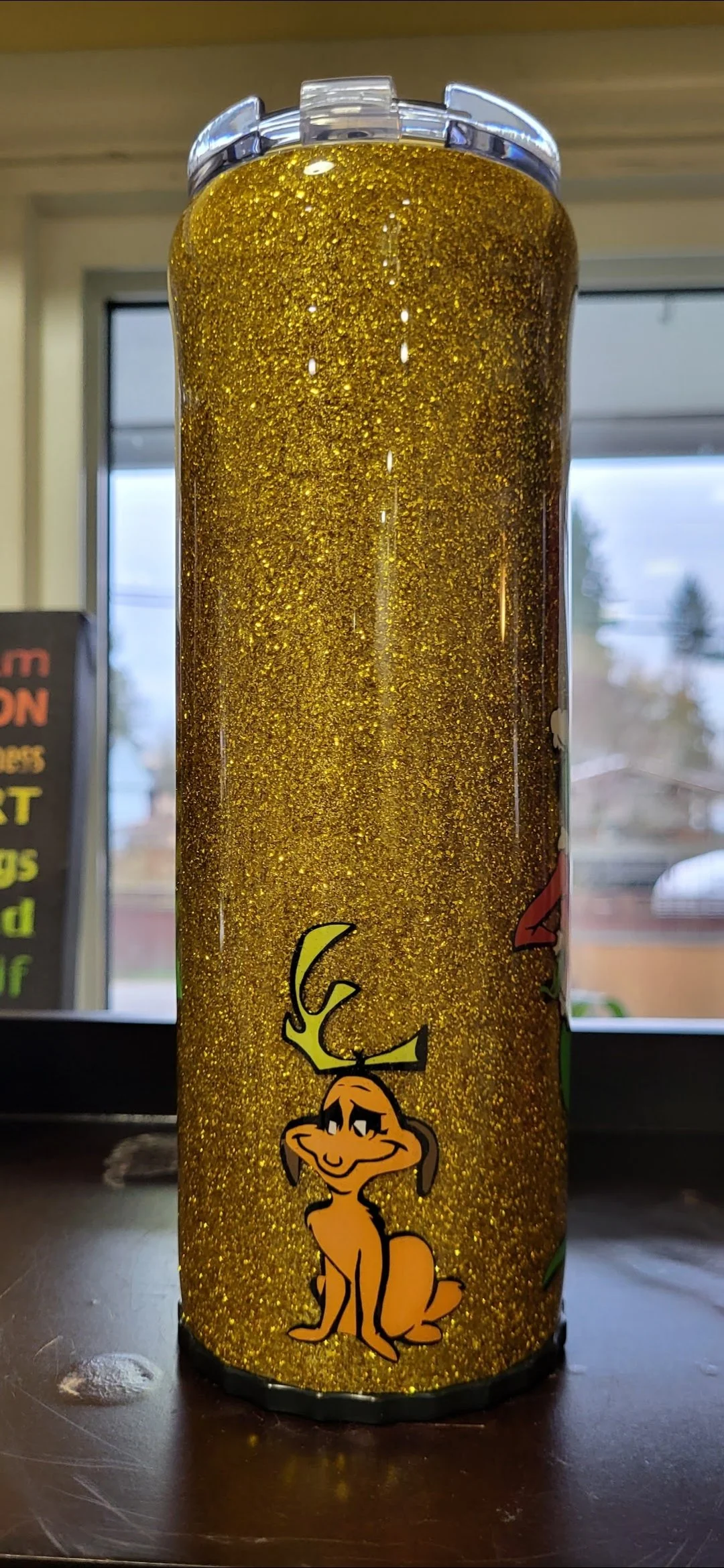 A tall container with a cartoon illustration of a smiling deer with antlers on a glittery gold background.