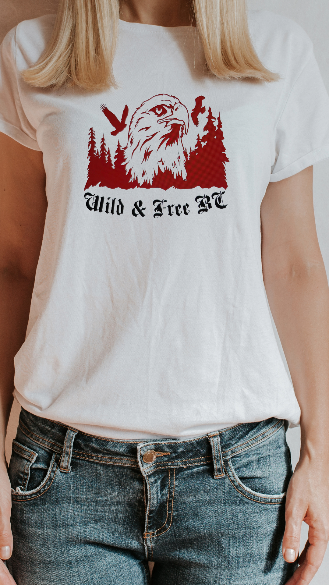 A woman wearing a white T-shirt with a design of an eagle, trees, and vultures, and text that reads 'Wild & Free BC'.