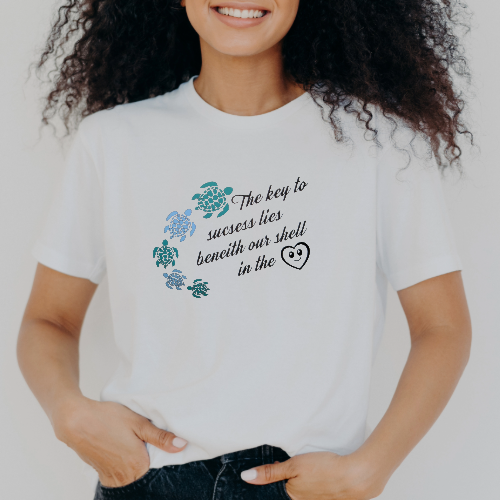 Close-up of a smiling woman wearing a white t-shirt with turtle graphics and the text: 'The key to success lies beneath our shell in the...'