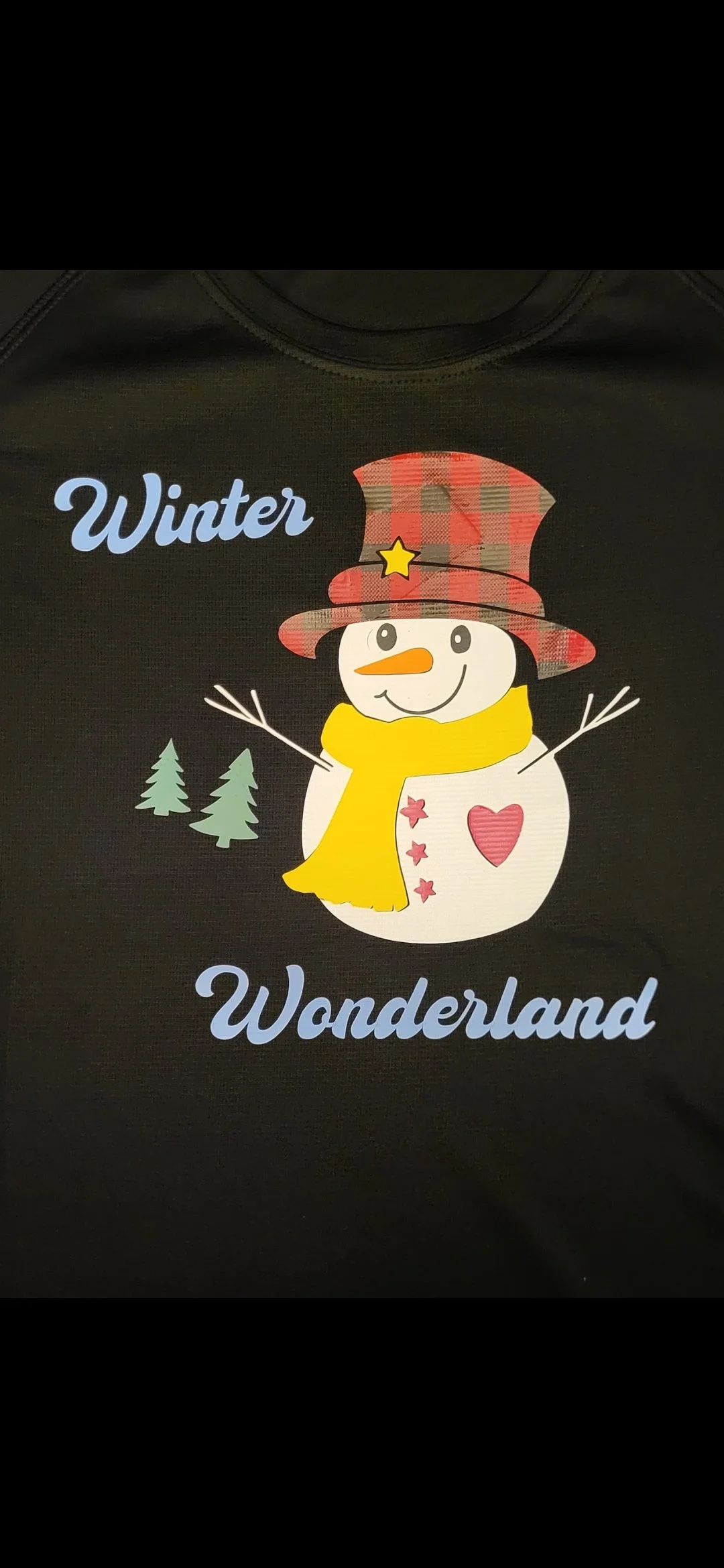 A cartoon snowman wearing a red plaid top hat with a yellow star, a yellow scarf, and a pink heart on its body, with green pine trees in the background and the words "Winter Wonderland" in blue.