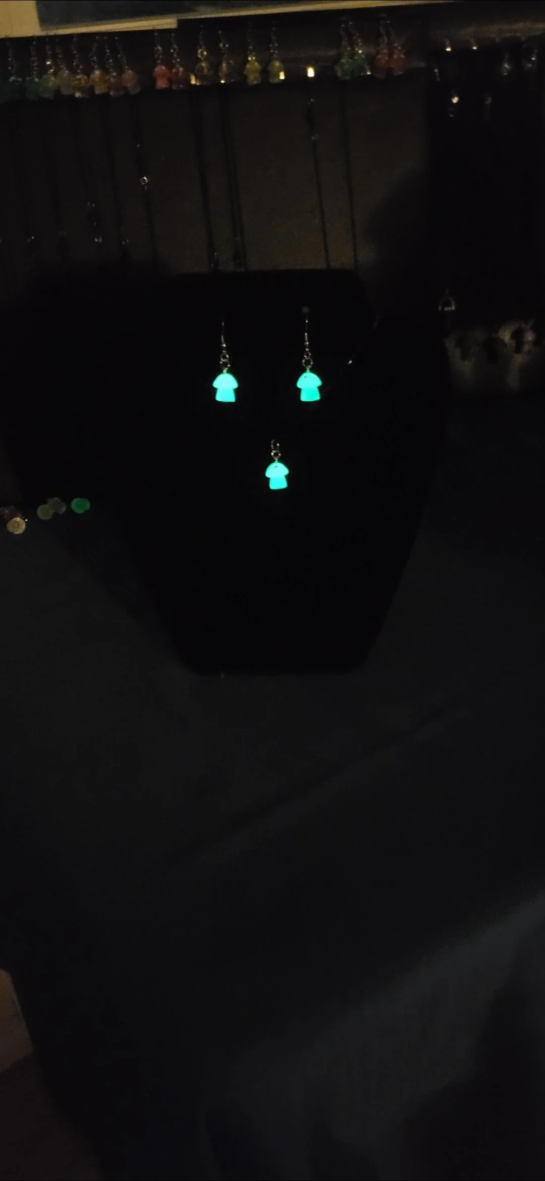 Glowing turquoise jewelry pieces, including earrings and a pendant, displayed on a black stand with a dark background.