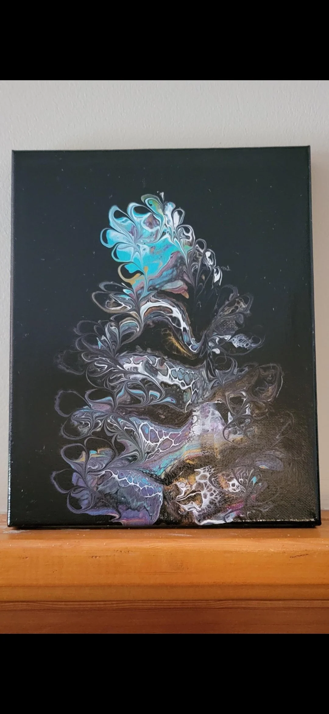 Abstract acrylic painting featuring swirling patterns in black, white, blue, purple, and hints of yellow on a black background, mounted on a wall above a wooden surface.