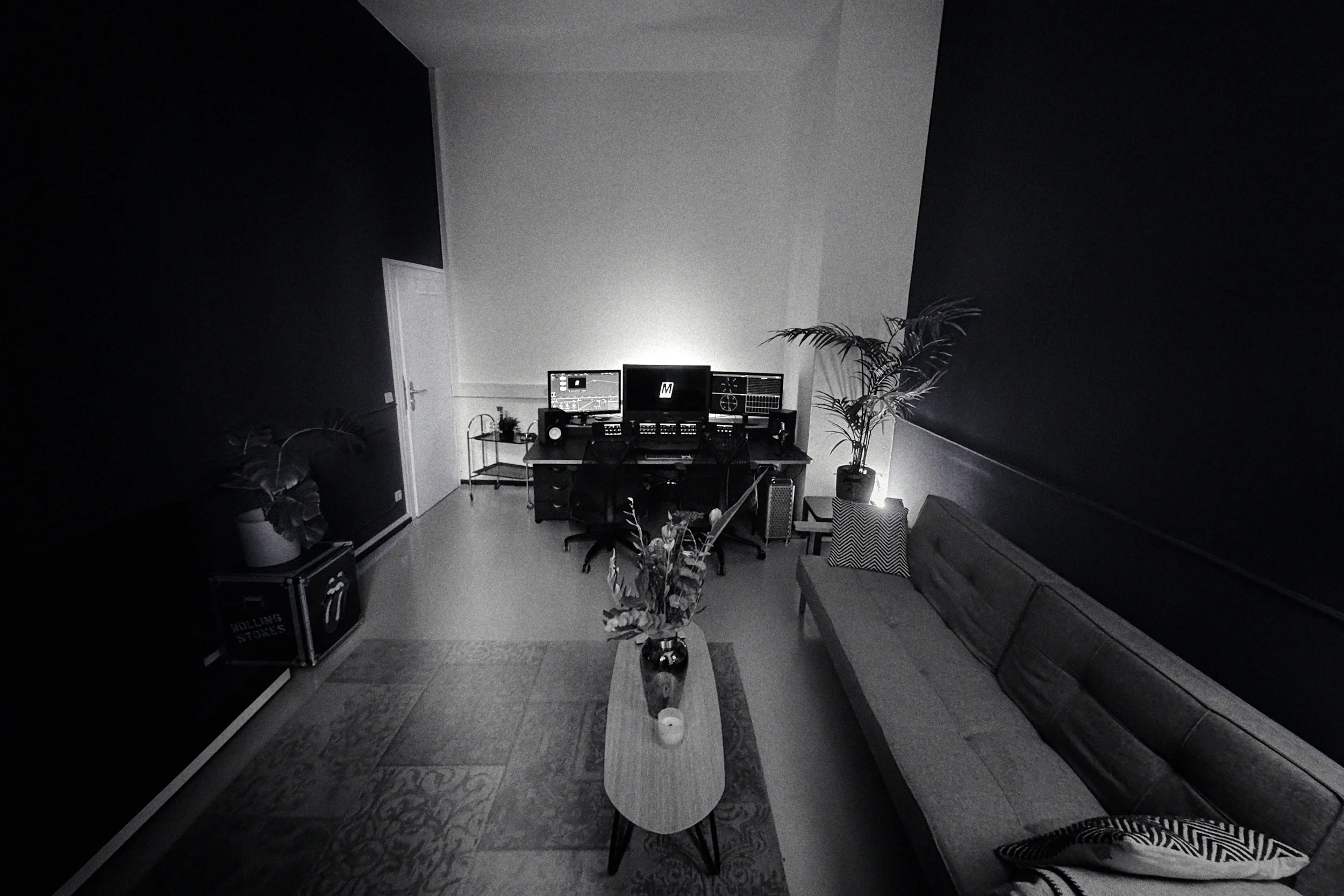 Suite 3 of MOGRADE's post-production studio, furnished with a sofa, a coffee table with plants and candles, and a desk with multiple monitors, panels and speakers.